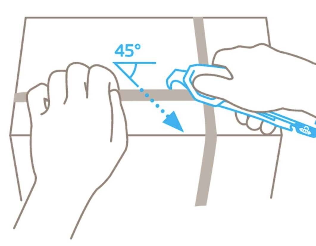Une main tient un carton tandis que l'autre découpe le carton le long d'une ligne à 45 degrés avec un cutter.