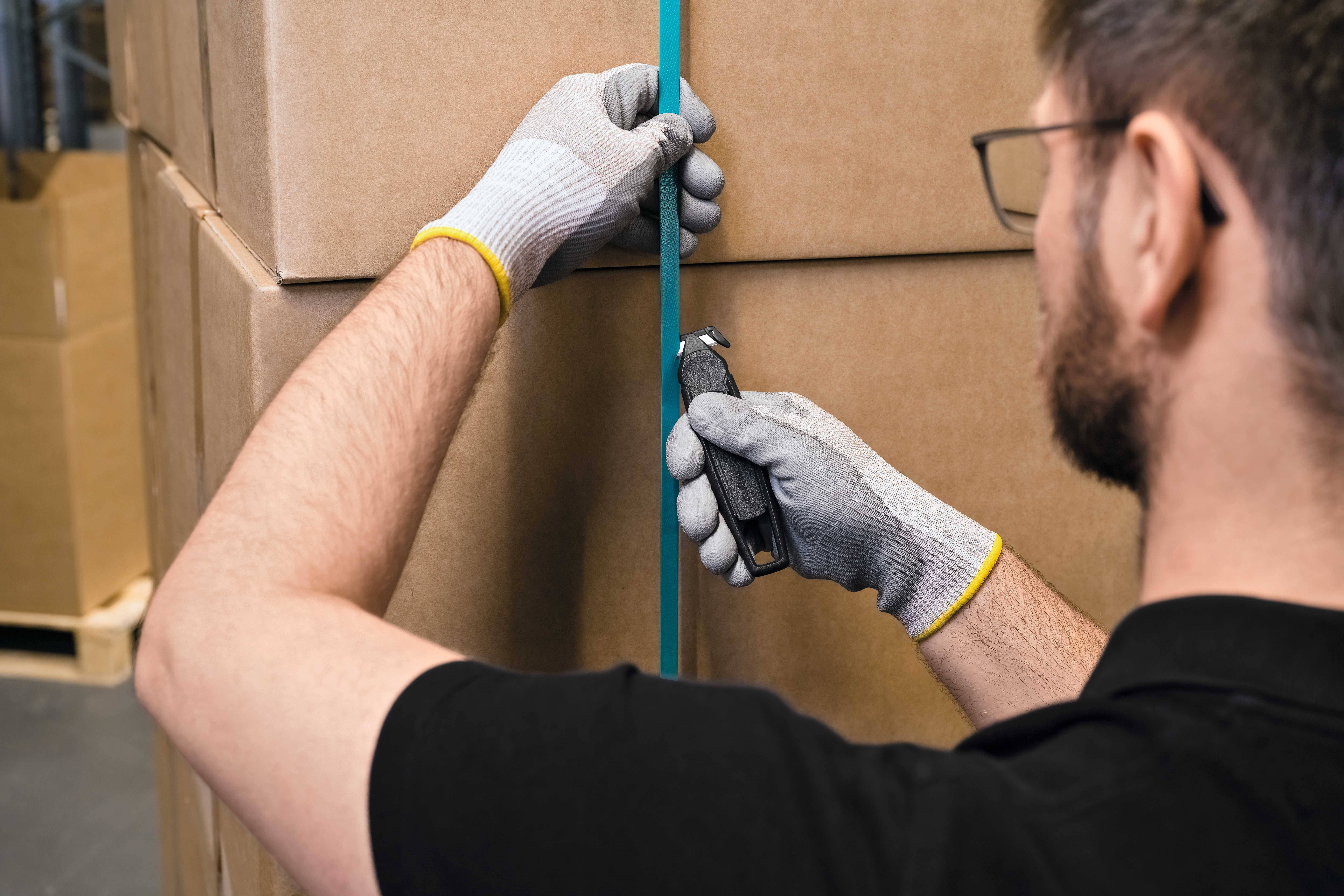 Une personne portant des gants ouvre un paquet enrubanné de bleu à l'aide d'un cutter.