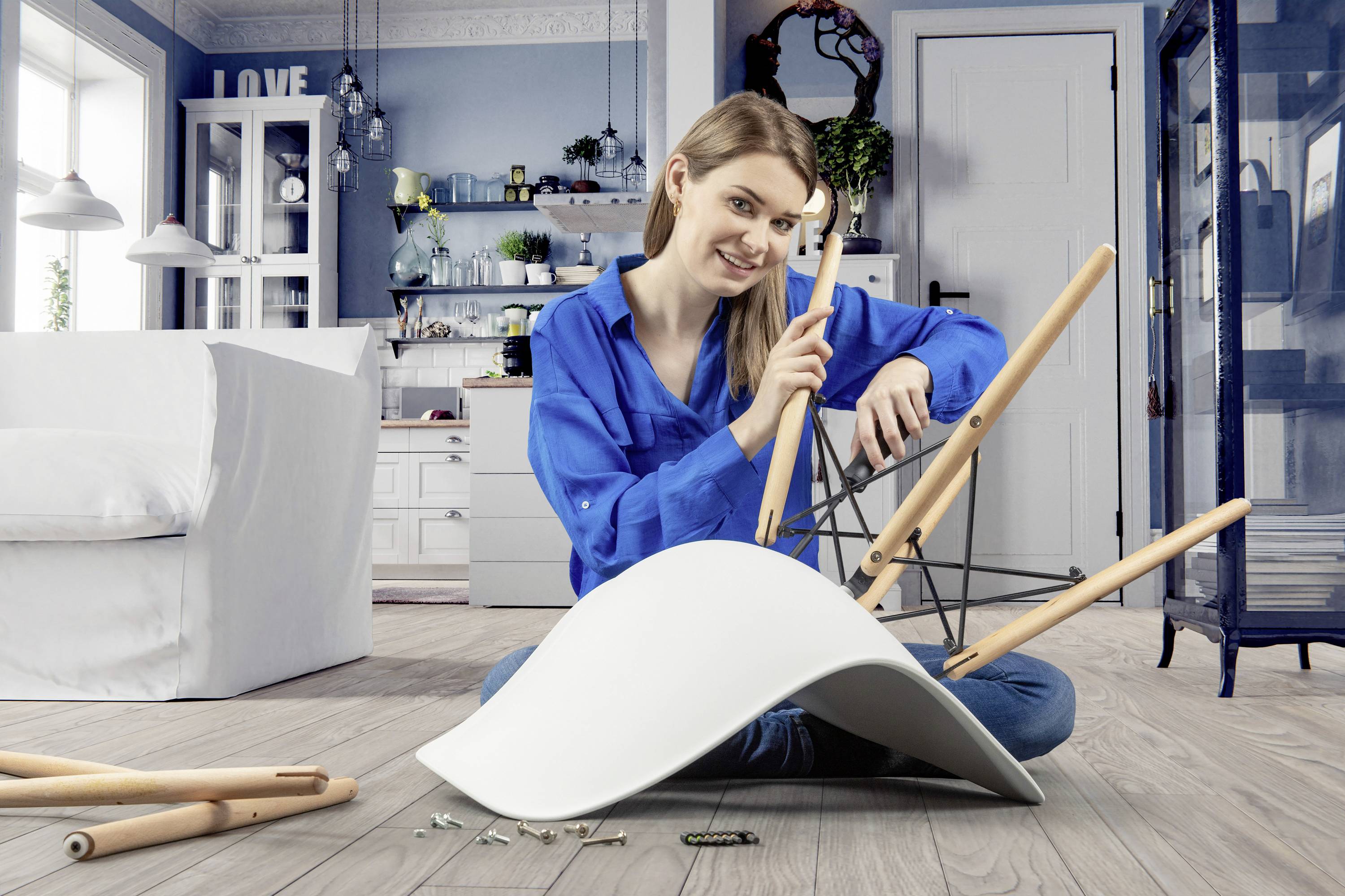 Une femme portant une chemise bleue est assise par terre et monte un chaise blanche dans un salon au design moderne.