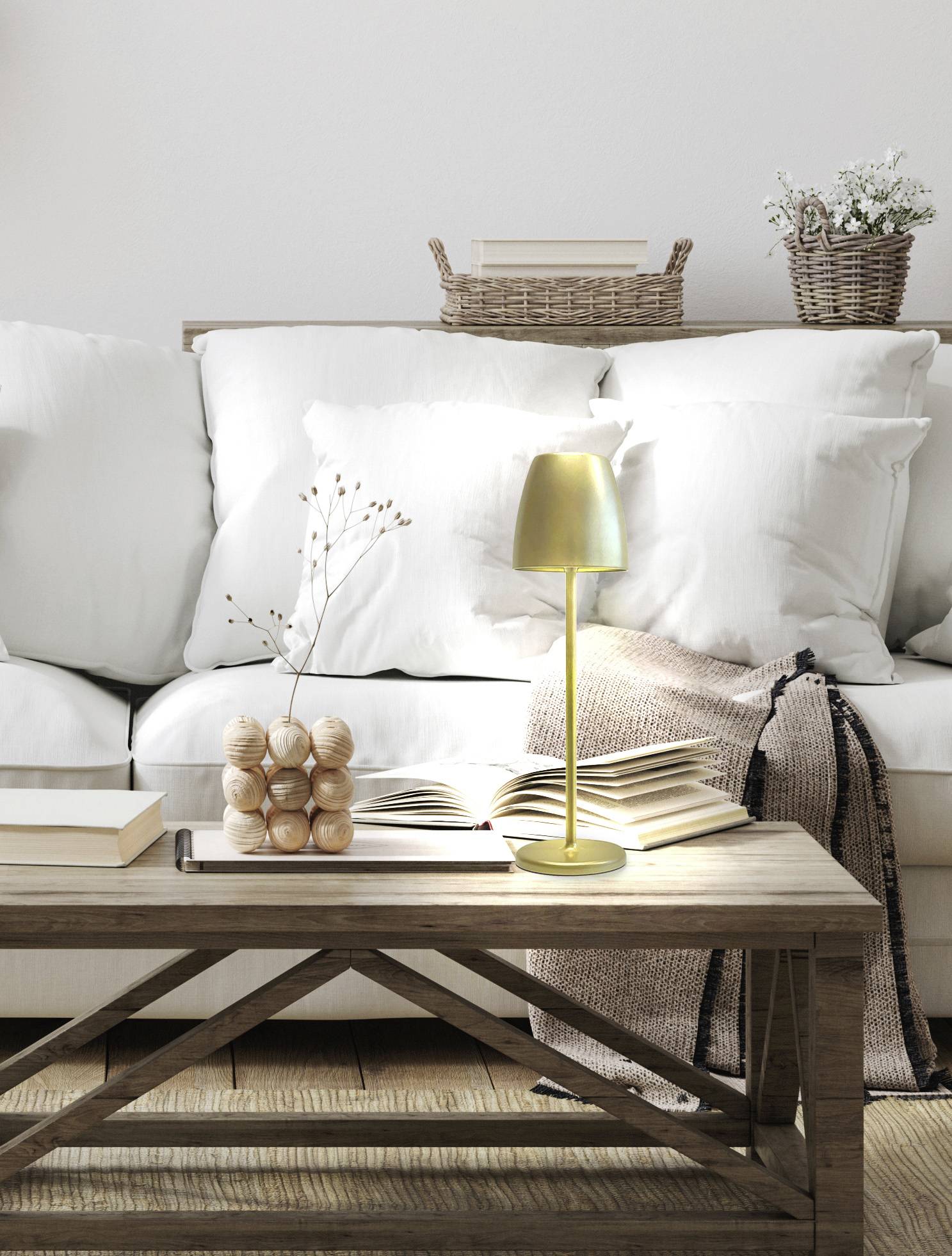 Salon avec un canapé blanc, une table en bois, sur laquelle se trouve une lampe dorée, des livres et des décorations. À l'arrière-plan, des paniers tressés.