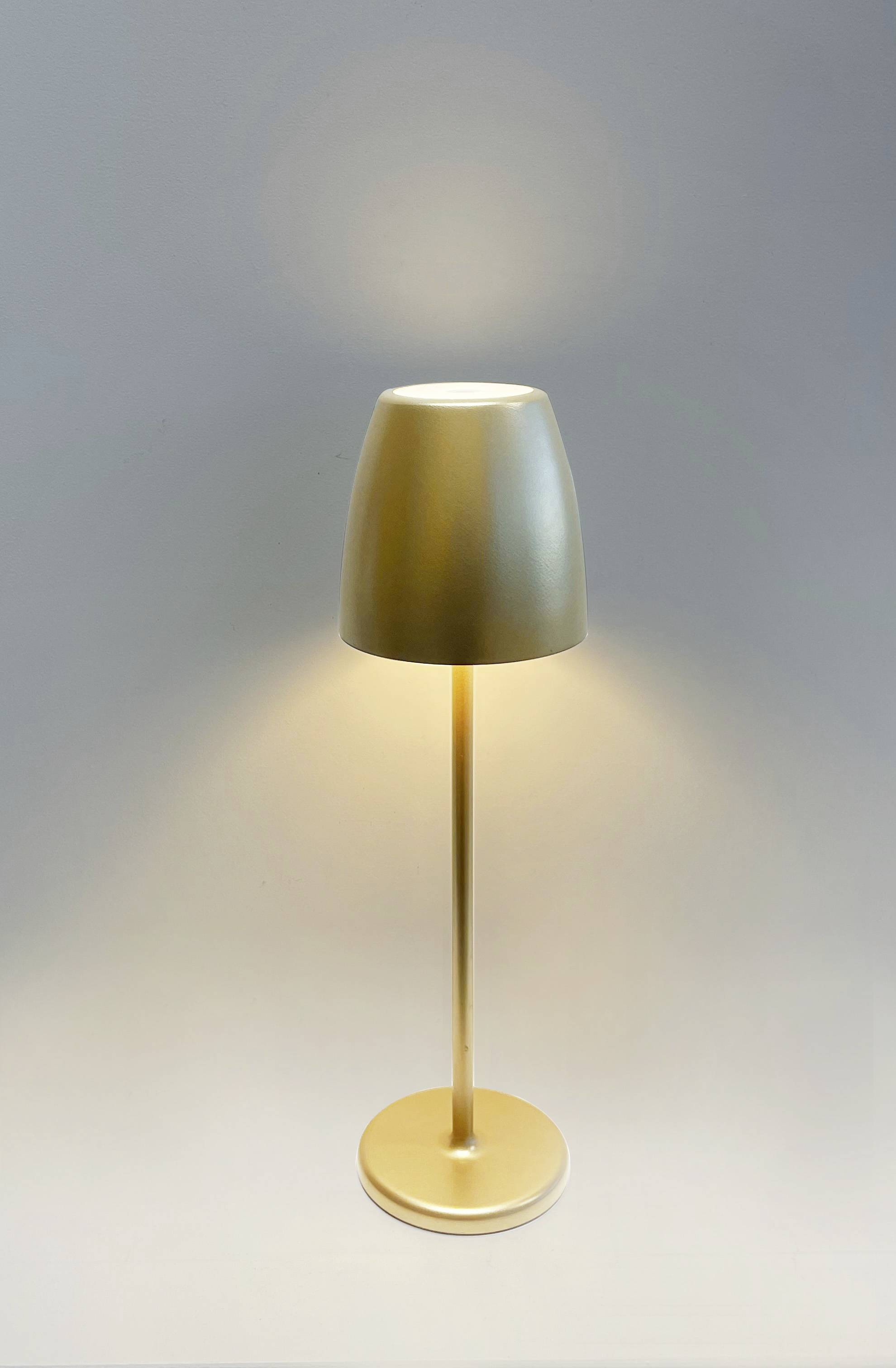 Lampe de table dorée à socle cylindrique et abat-jour conique qui diffuse une lumière douce dans un espace neutre.