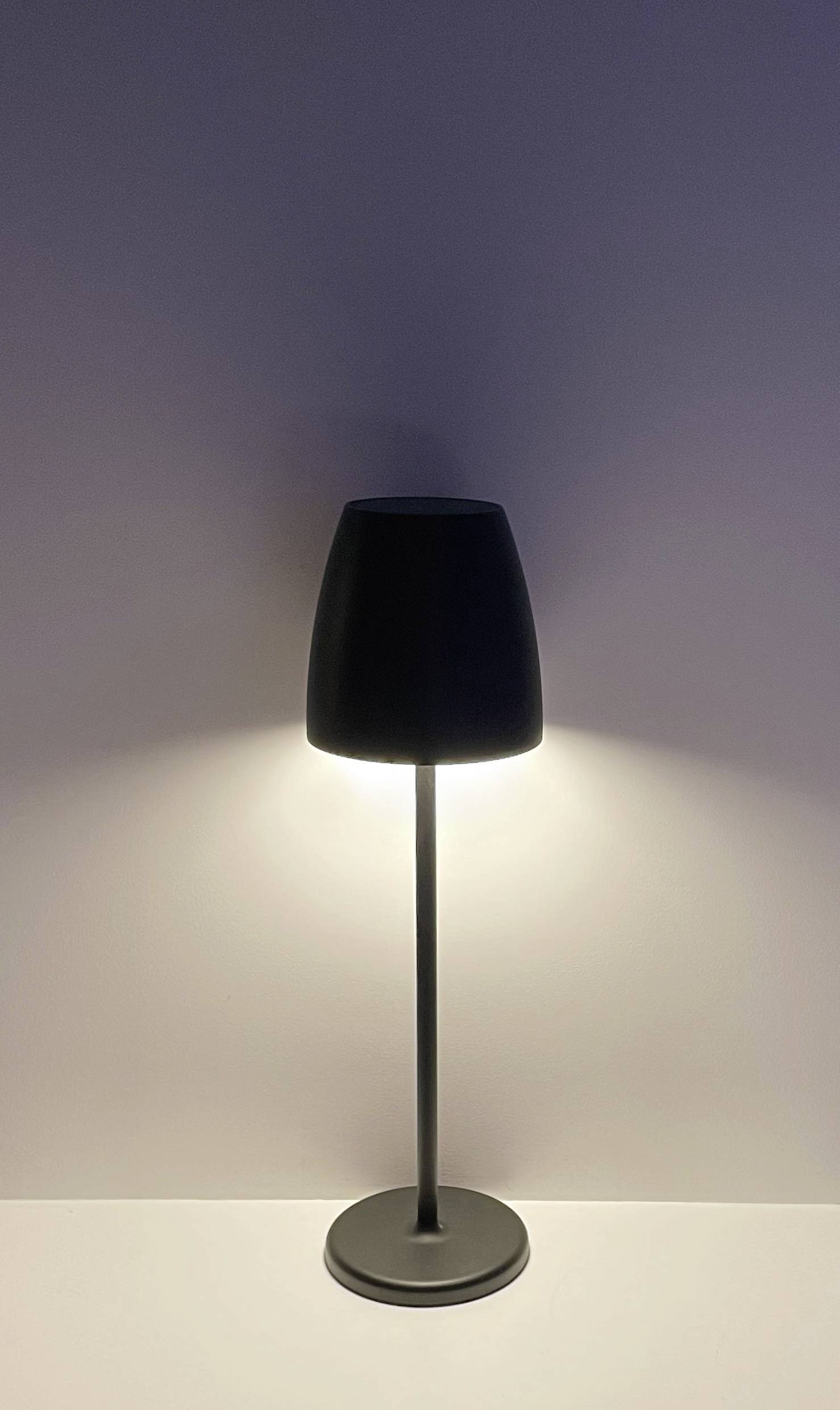 Une lampe sur pied noire illumine un mur blanc. La lumière rayonne vers le haut et vers le bas, créant un éclairage doux.