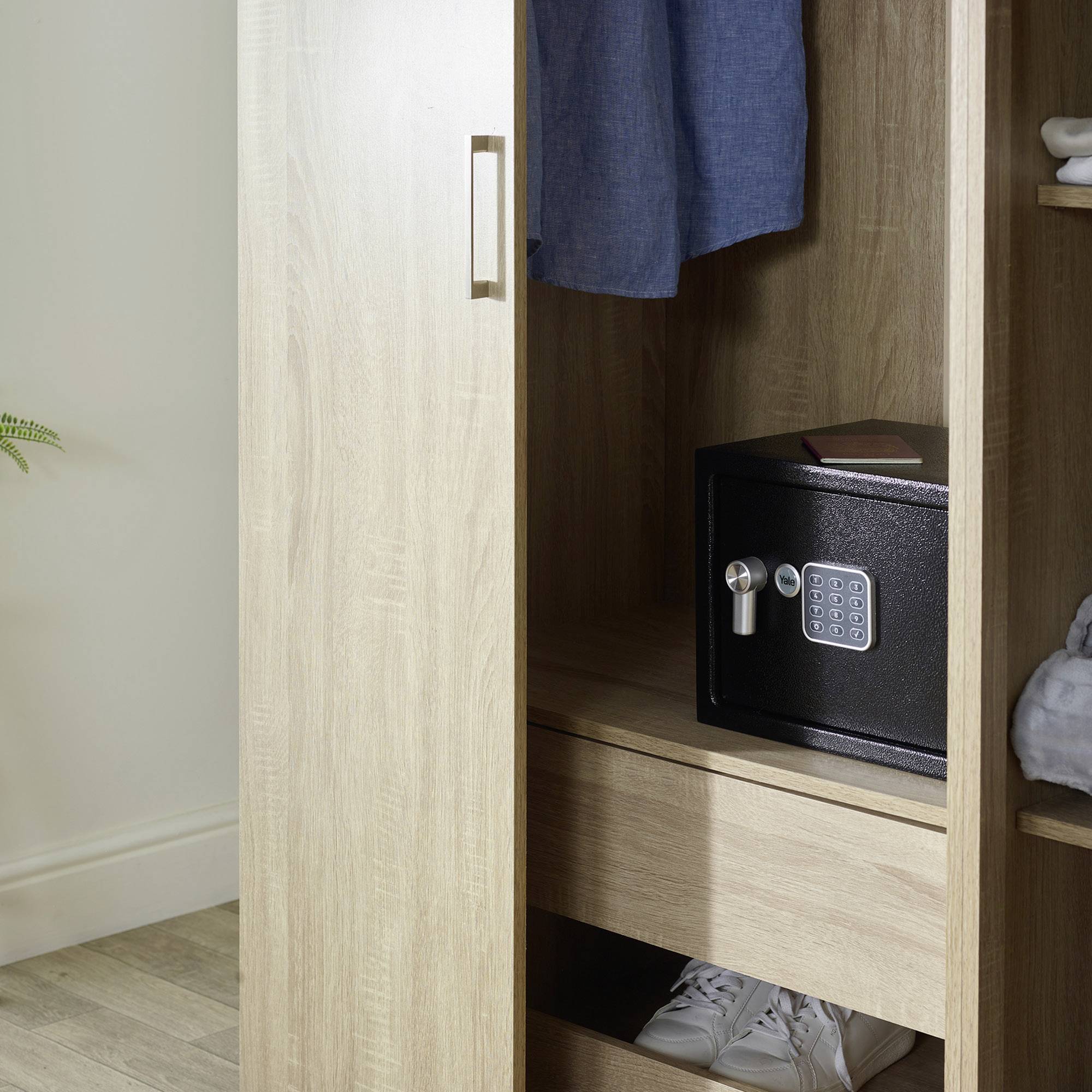 Un placard en bois ouvert montre un coffre-fort numérique sur une étagère. En dessous, il y a une paire de baskets blanches.