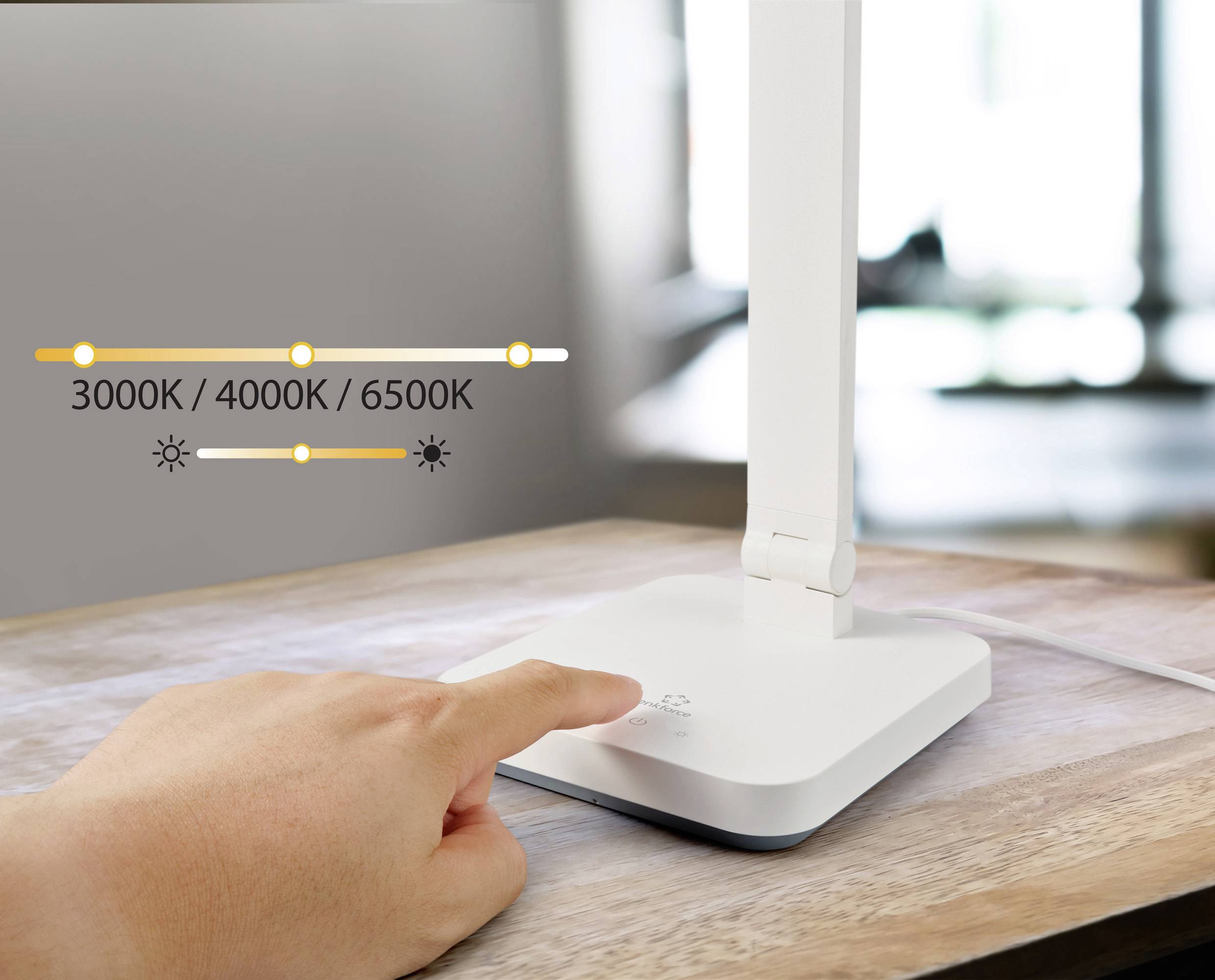 Une main touche la base d'une lampe de table blanche posée sur une table en bois. Un affichage montre différentes températures de couleur : « 3000K / 4000K / 6500K ».