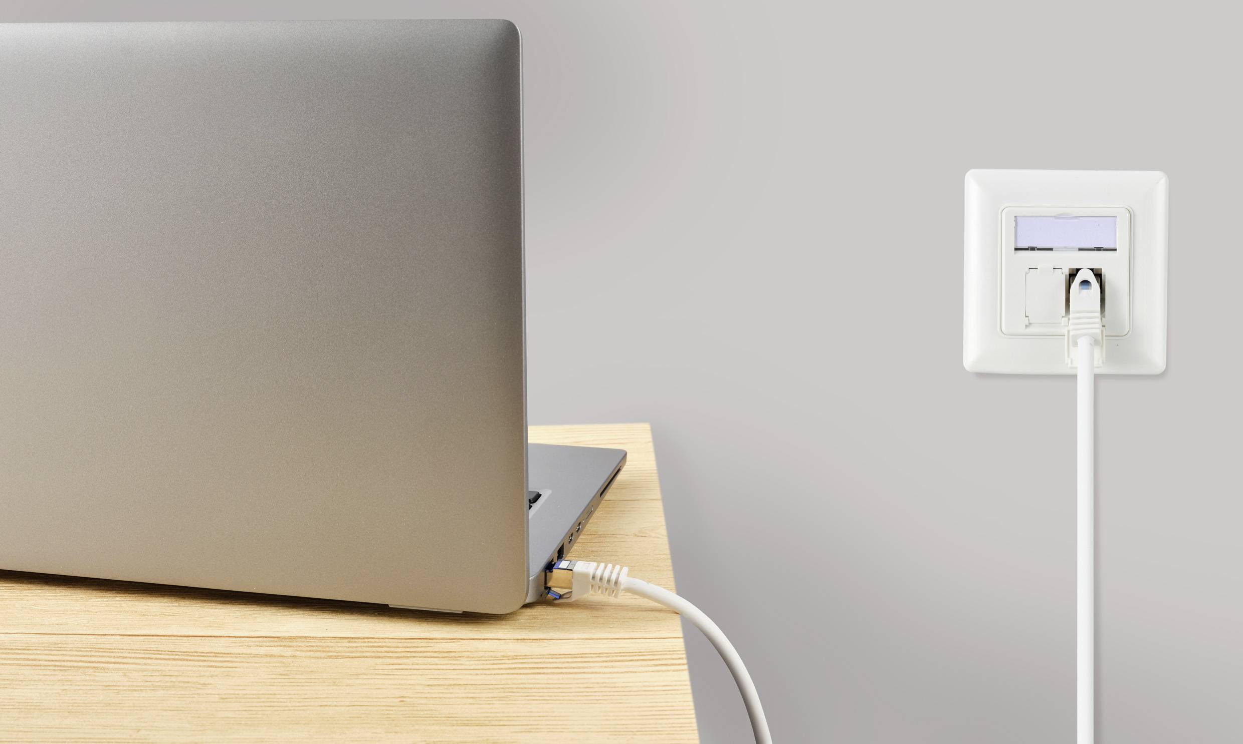 Un ordinateur portable est connecté à une prise murale par un câble réseau, adapté aux connexions internet.