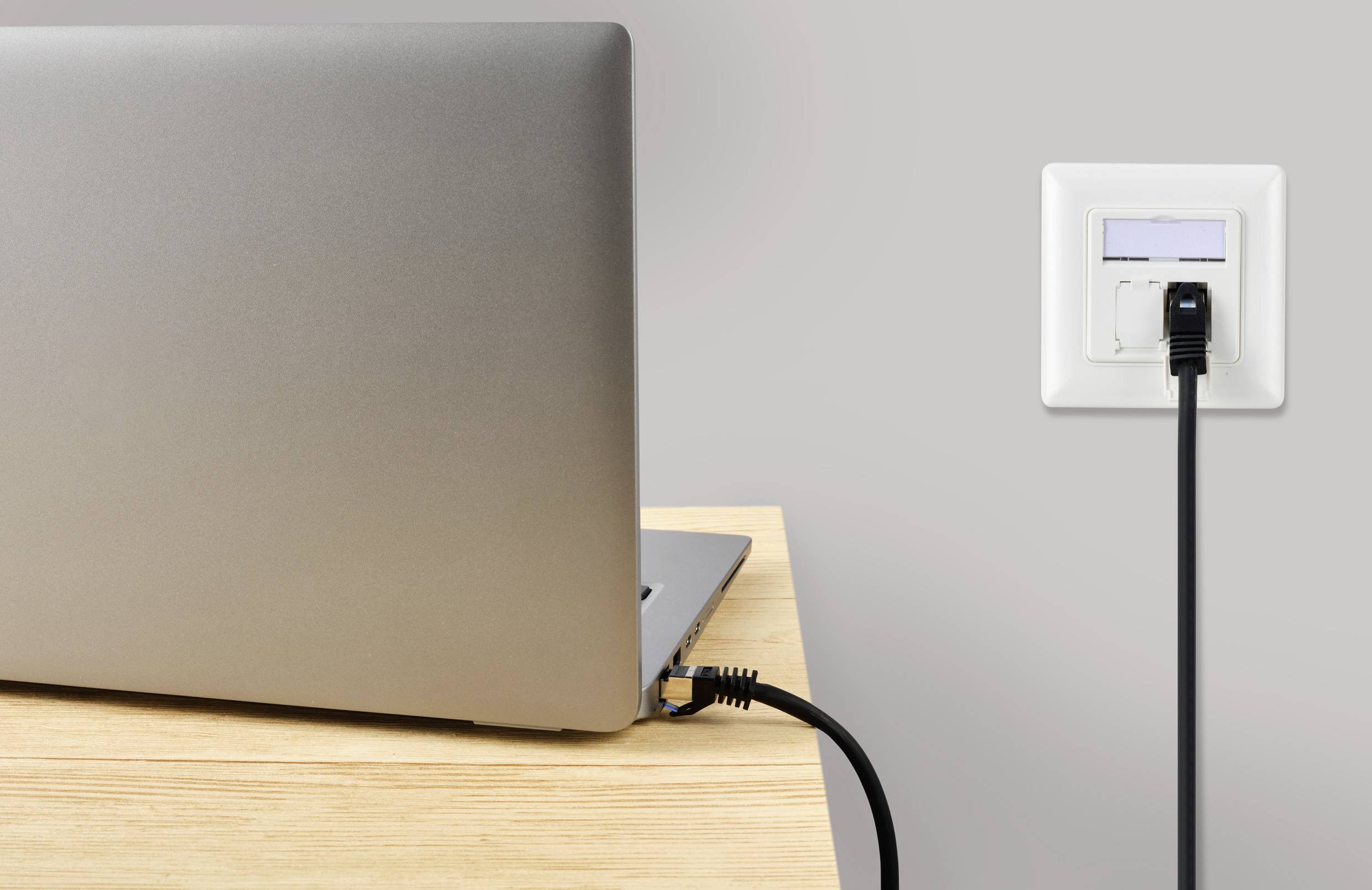 Un ordinateur portable posé sur une table est connecté à une prise murale par un câble réseau.