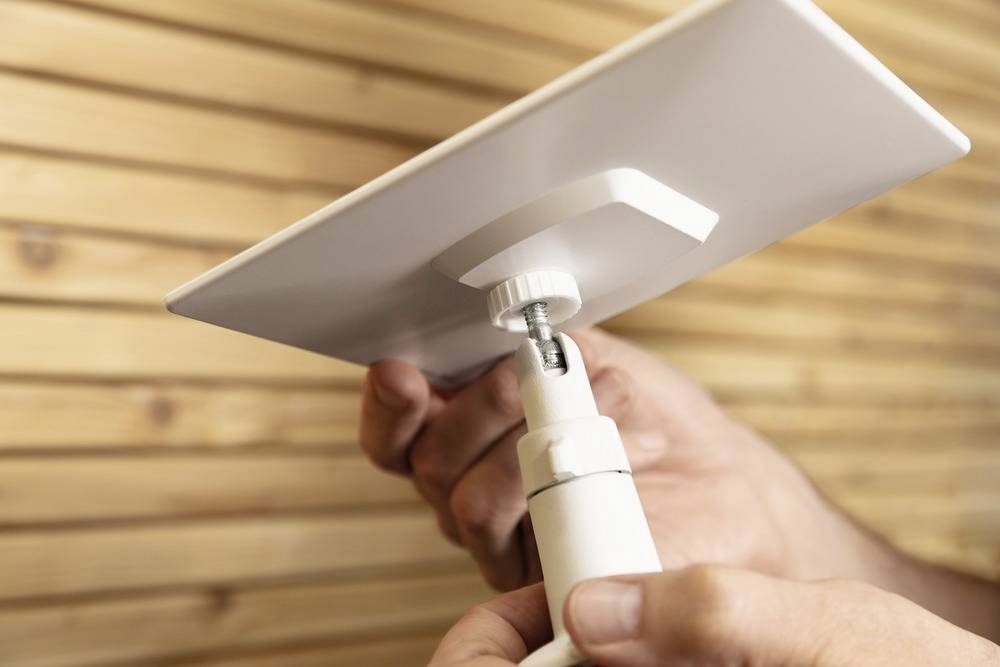 Une personne fixe un panneau solaire rectangulaire blanc sur un support ajustable devant un mur en bois.