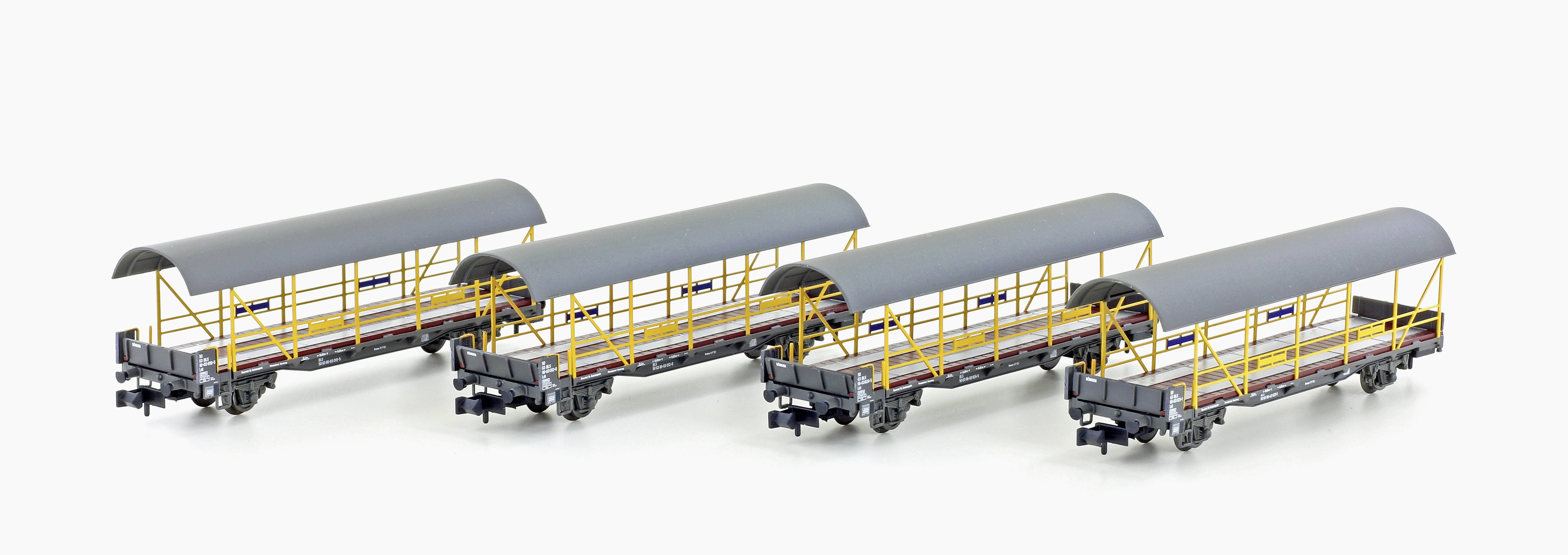 Quatre wagons de marchandises gris ouverts avec des toits bombés sont alignés côte à côte sur des rails. Ils ont des garde-corps jaunes et paraissent propres.