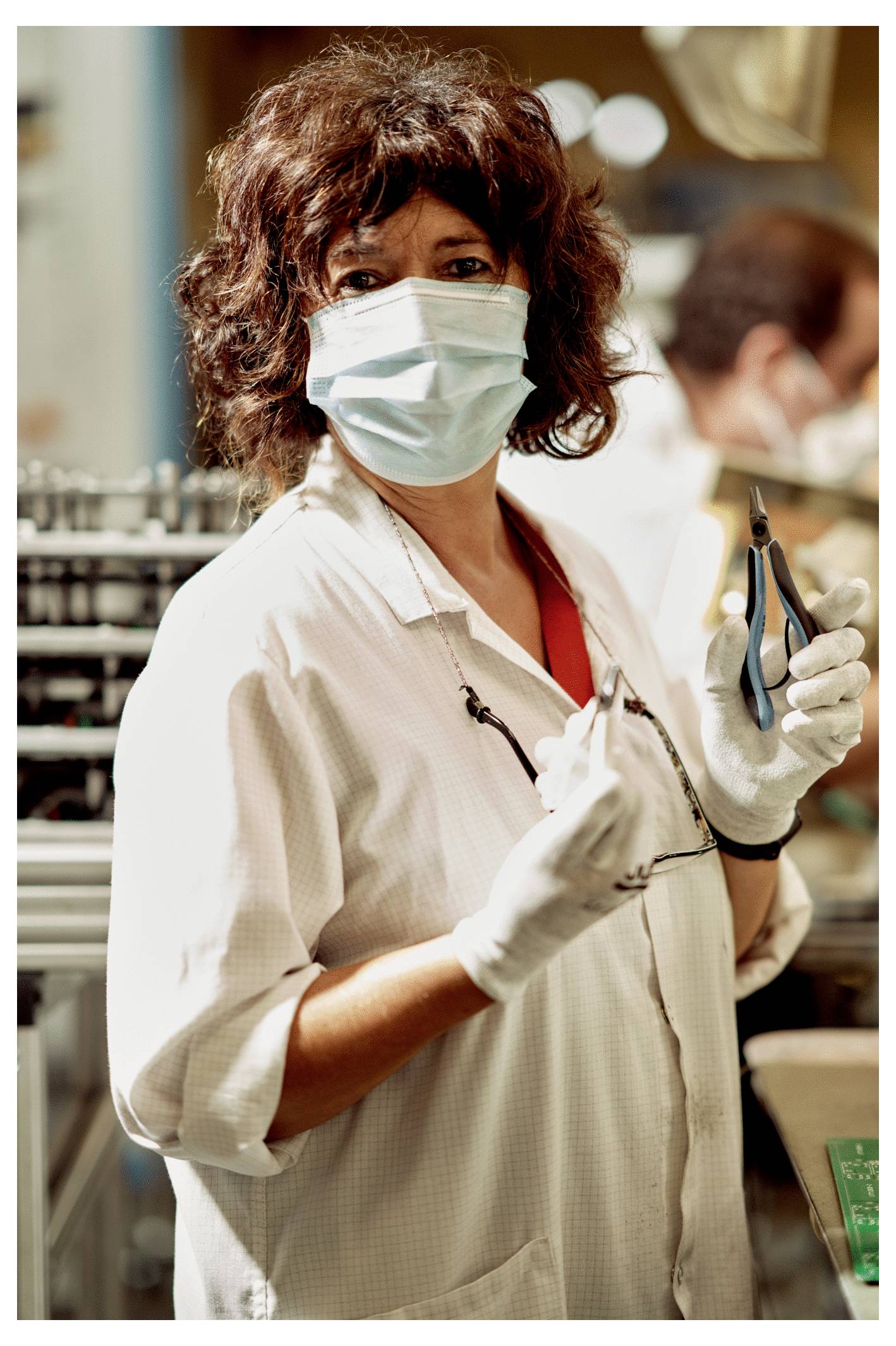 A person wearing a mask and gloves holds tools, standing in what appears to be a workshop or lab environment, looking at the camera.
