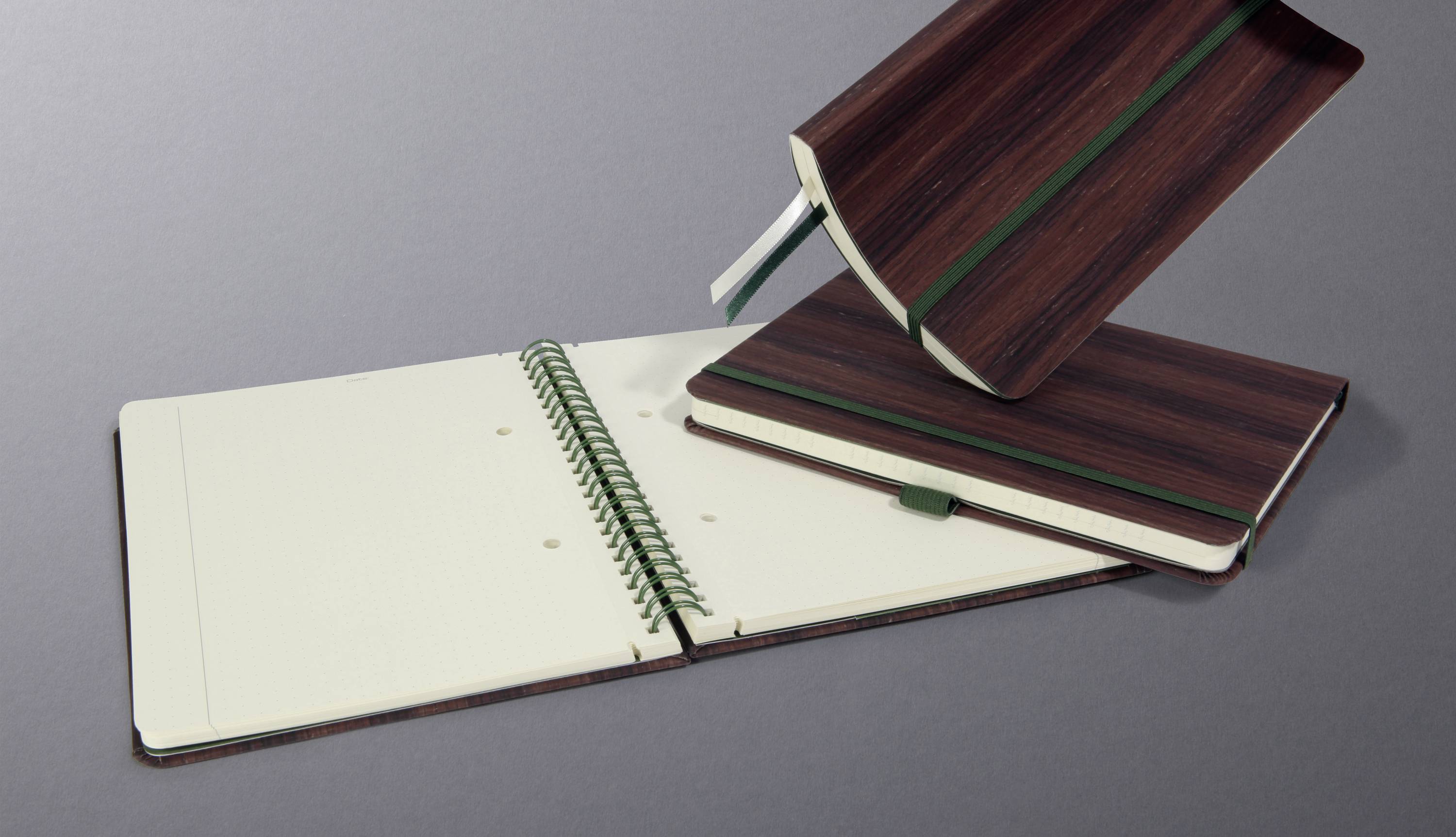 Trois carnets sur un fond gris. L'un est ouvert, le deuxième est fermé, et le troisième est tenu ouvert. Tous ont une couverture brune.