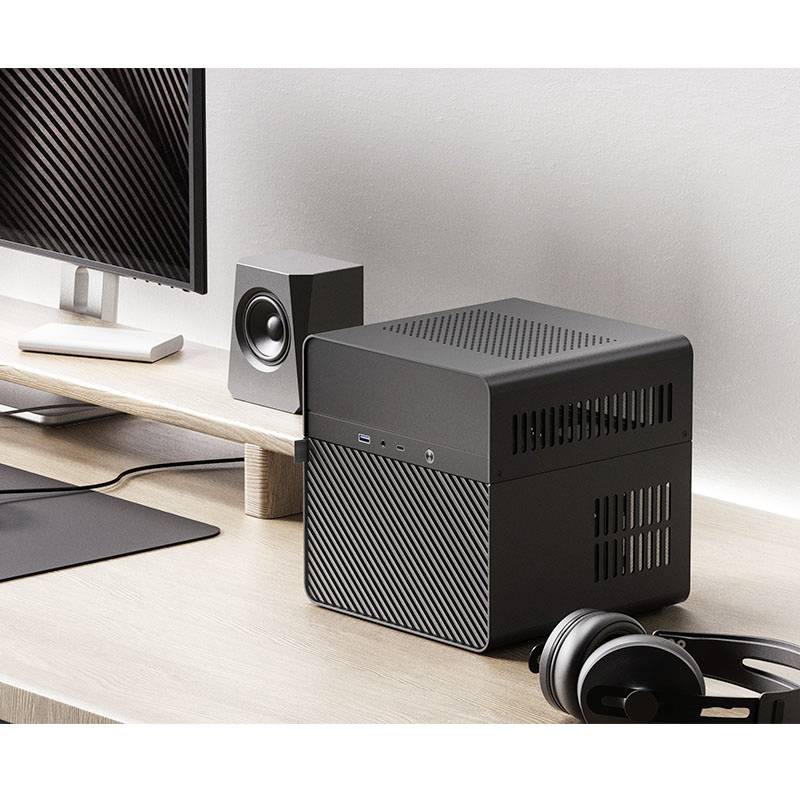 Sur un bureau, un mini-PC noir moderne est posé à côté d'écouteurs et d'enceintes. Un écran est visible à proximité.