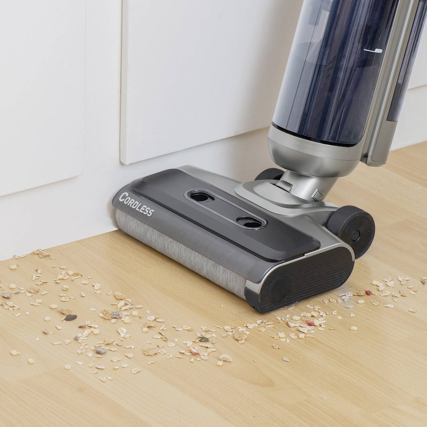 Un aspirateur sans fil nettoie un parquet, aspirant des miettes et de la saleté.
