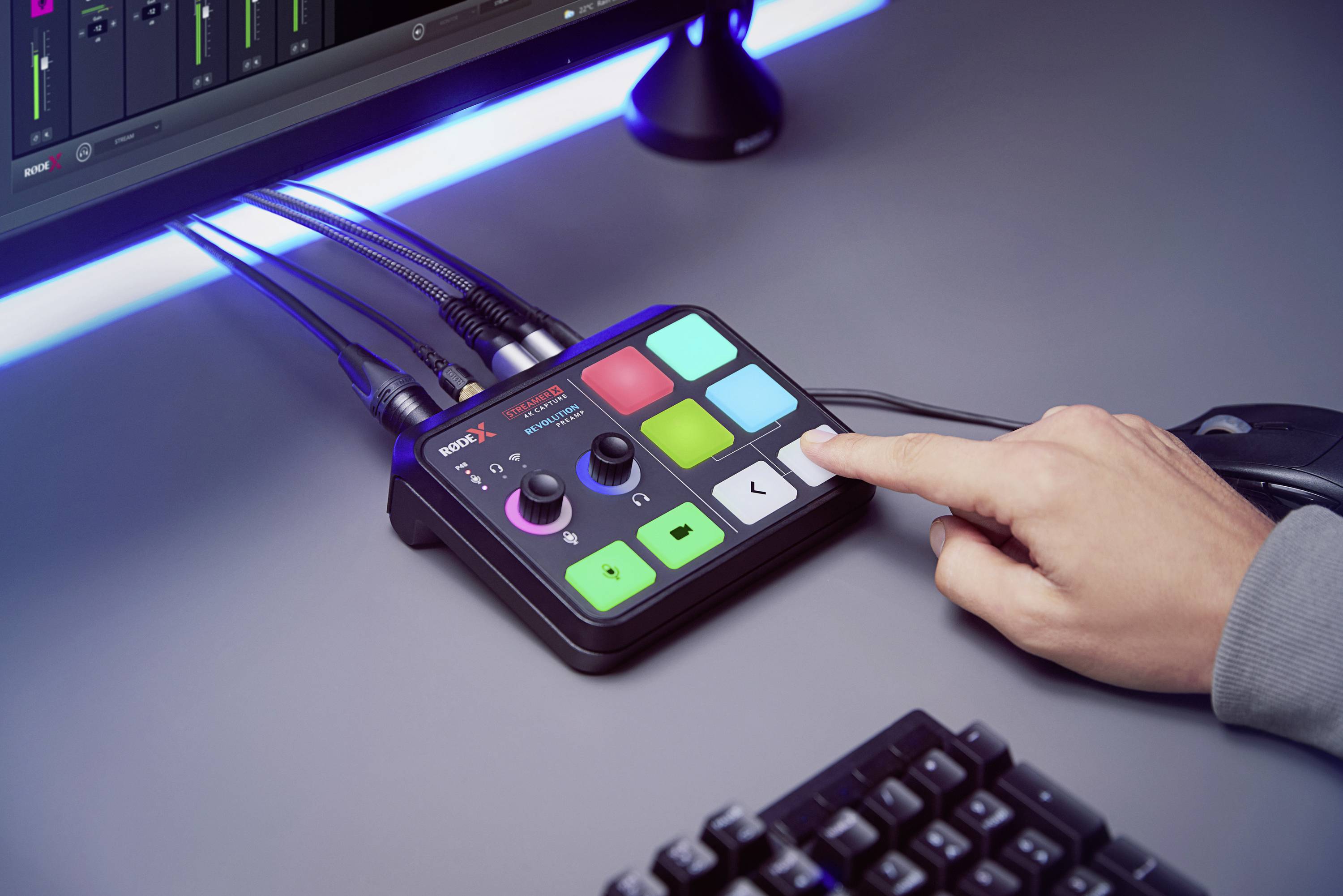 Une personne appuie sur une touche d'une console de mixage audio à côté d'un écran d'ordinateur. Des touches lumineuses et colorées s'illuminent sur l'appareil.