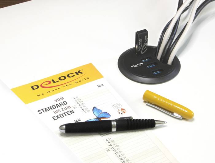 Une table avec un catalogue, un stylo à bille et un hub USB avec plusieurs câbles. Le catalogue porte le titre 'Du standard à l'exotique'.