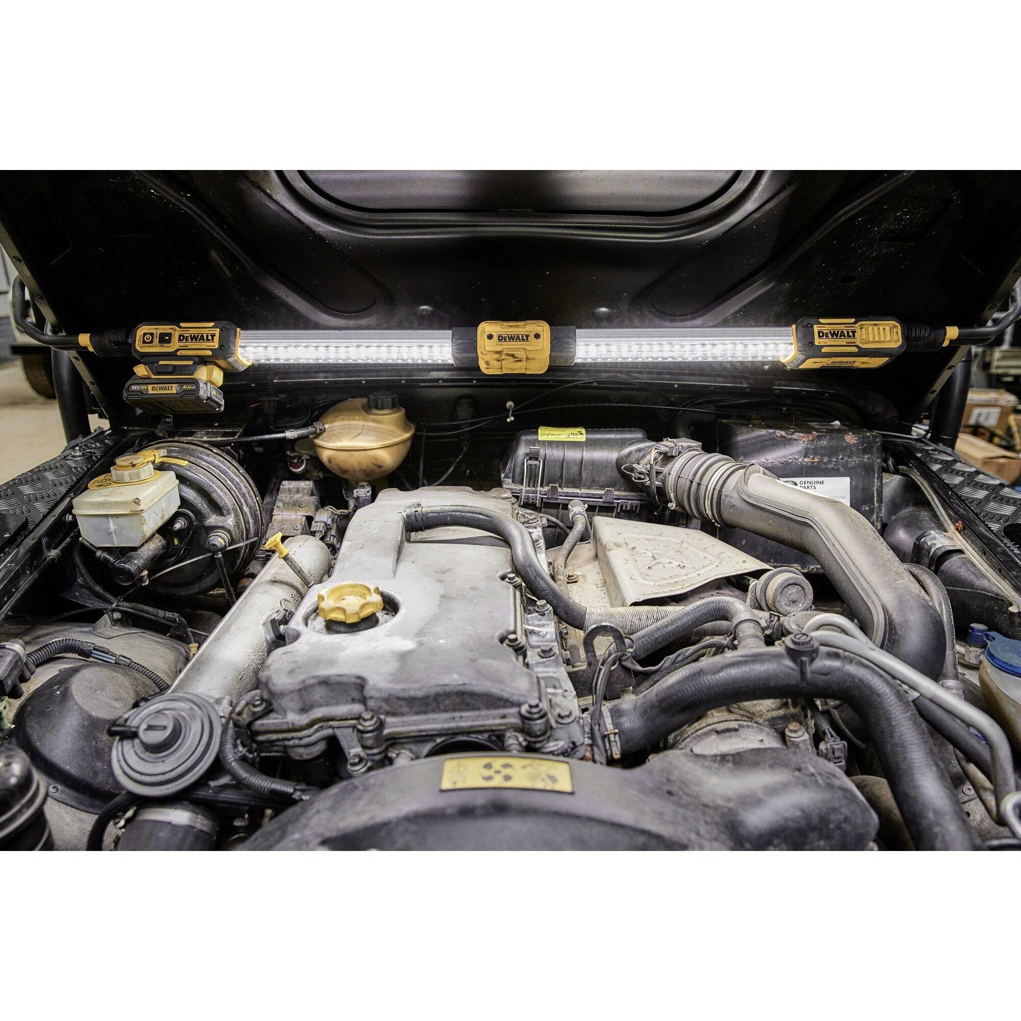 Un compartiment moteur ouvert d'une voiture, révélant des composants tels que des tuyaux, des réservoirs et des connexions, éclairé par plusieurs lampes.