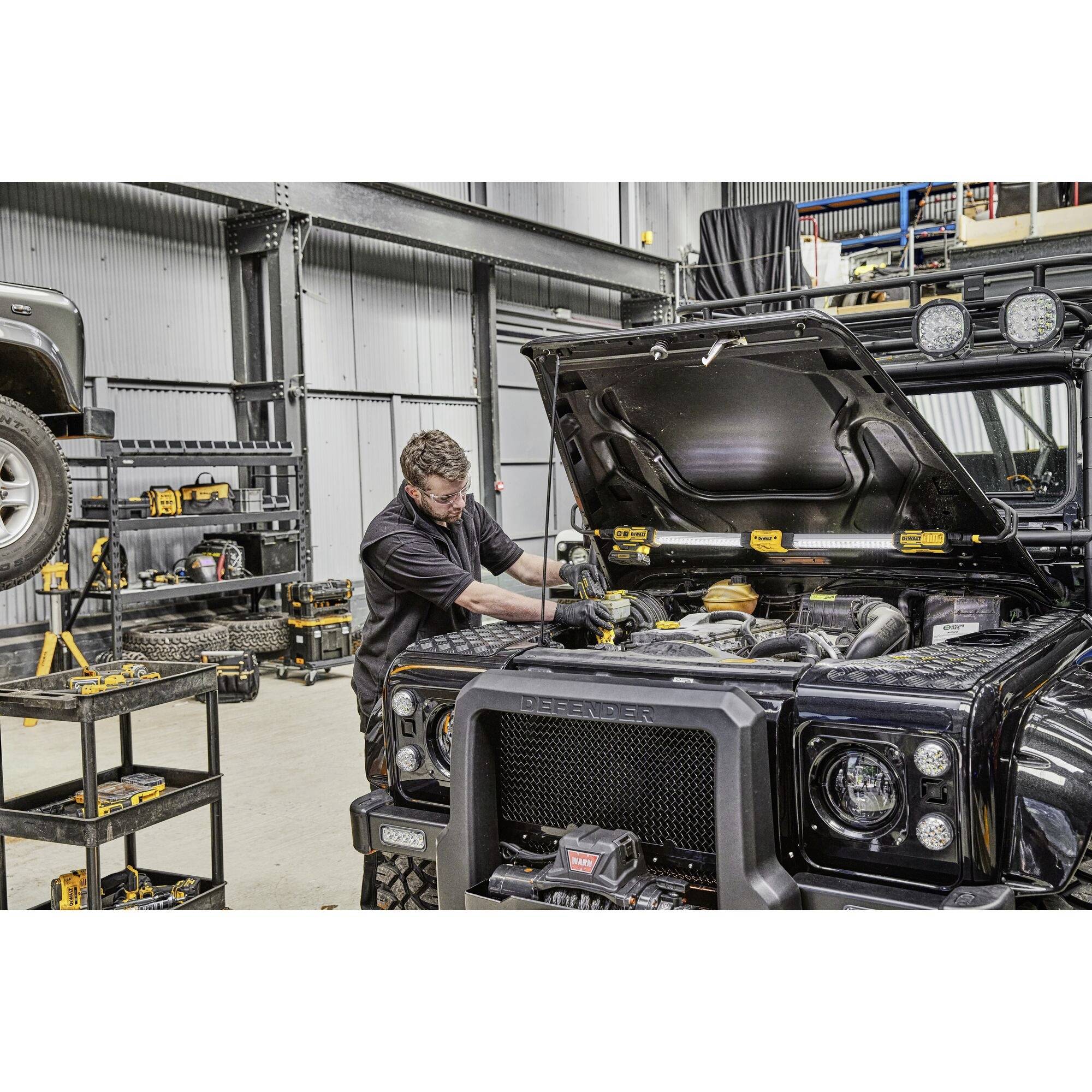 Un mécanicien travaille dans un atelier sur un SUV noir à capot ouvert. Des outils sont visibles en arrière-plan.