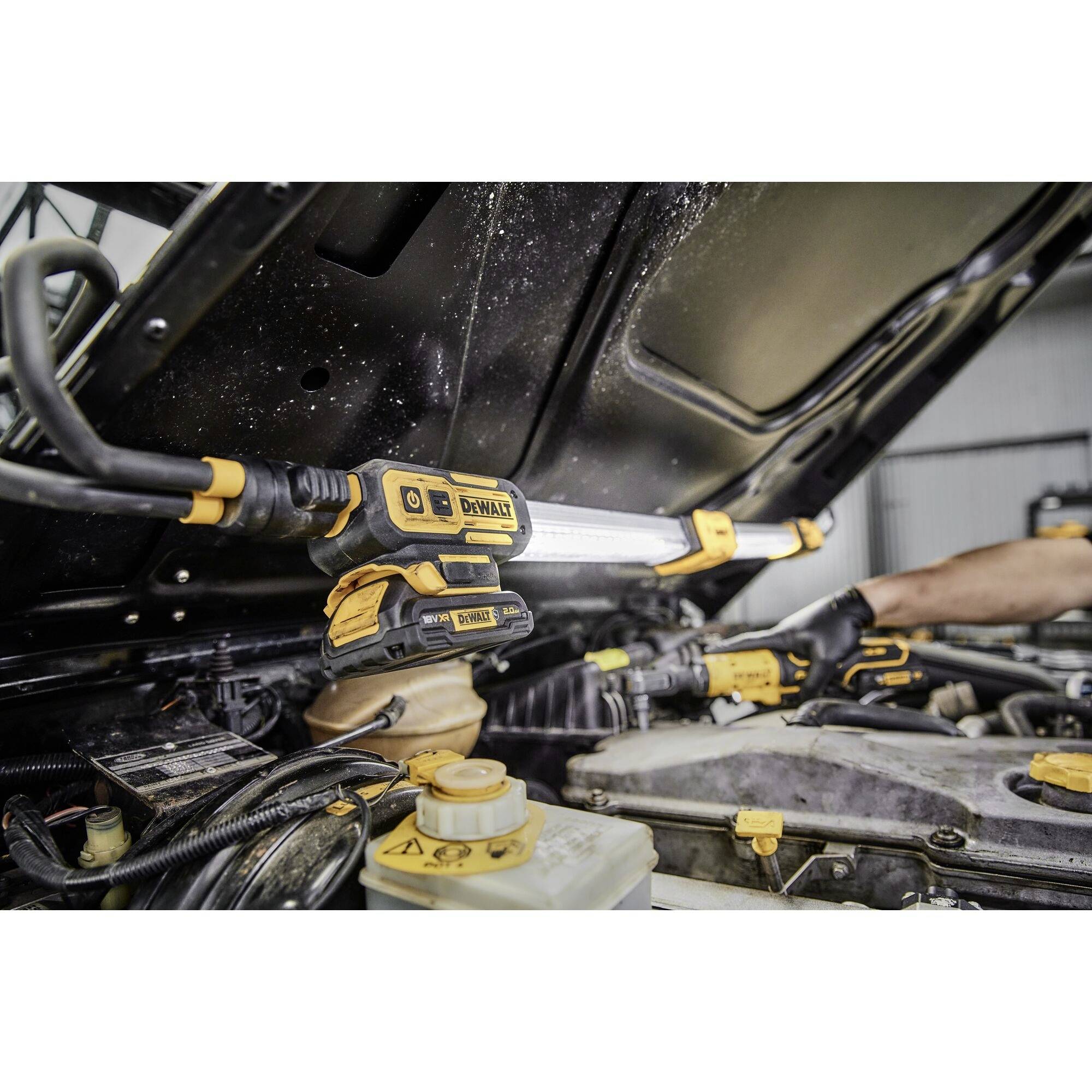 Un mécanicien répare le compartiment moteur d'un véhicule, portant des gants et utilisant une lampe de poche, entouré de diverses pièces et outils automobiles.