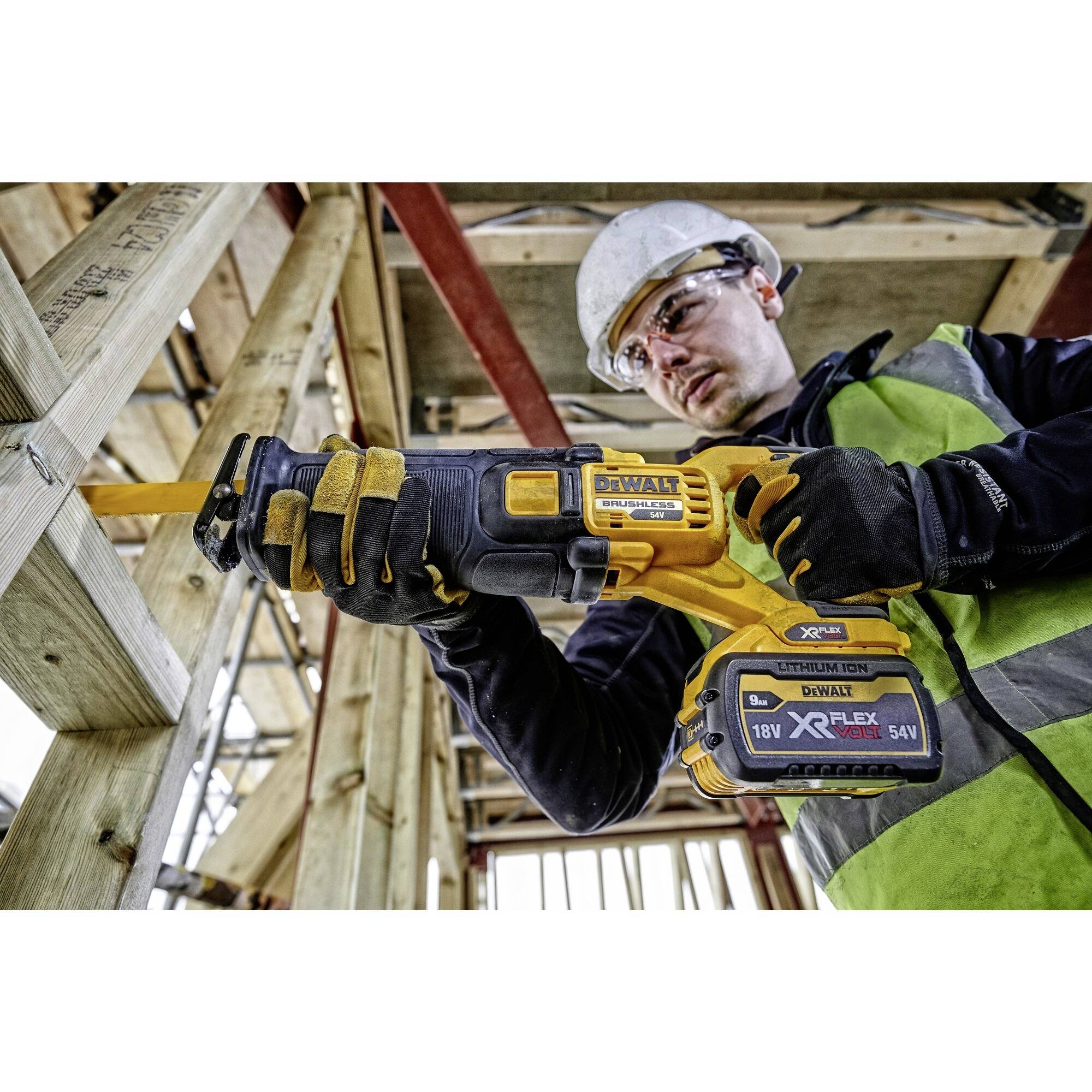 Un ouvrier portant un casque de chantier et un gilet de sécurité utilise une scie électrique pour couper des poutres dans un bâtiment.