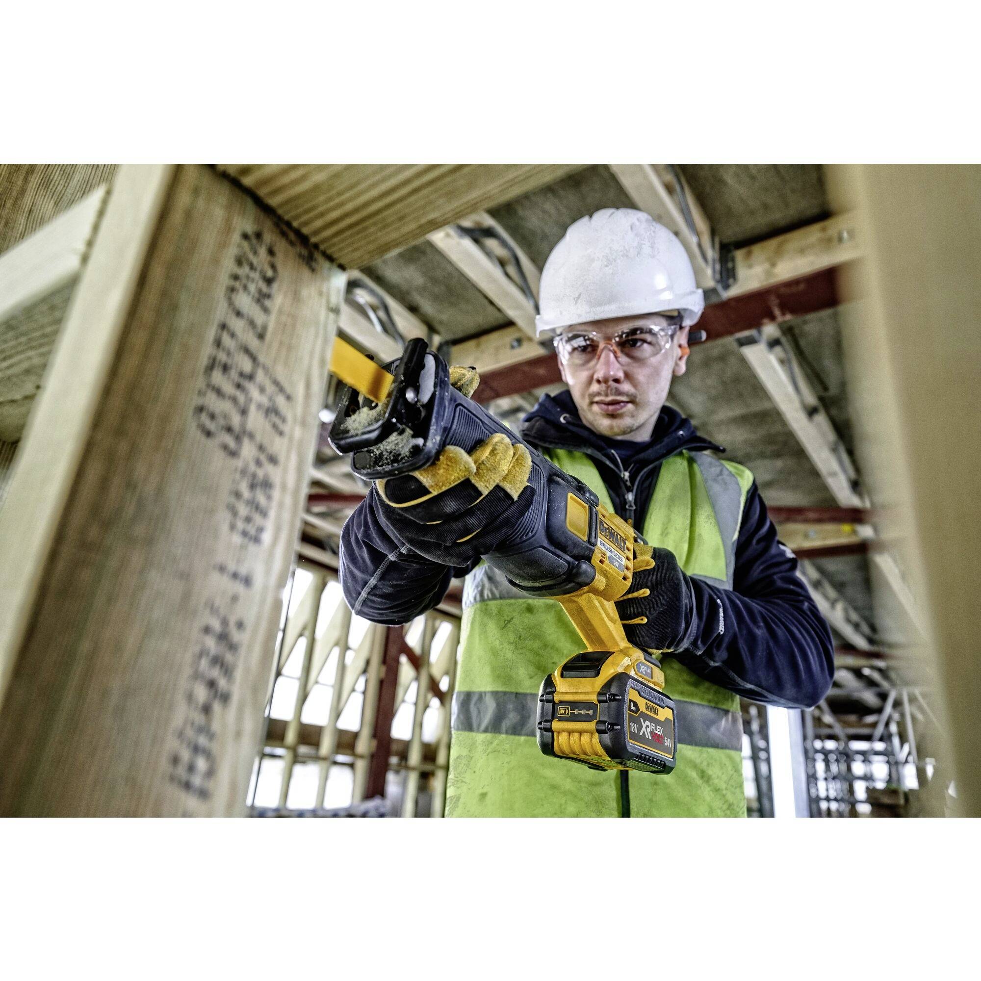 Un ouvrier portant un casque de sécurité et un gilet de protection utilise un outil électrique pour travailler une structure en bois dans un bâtiment en construction.