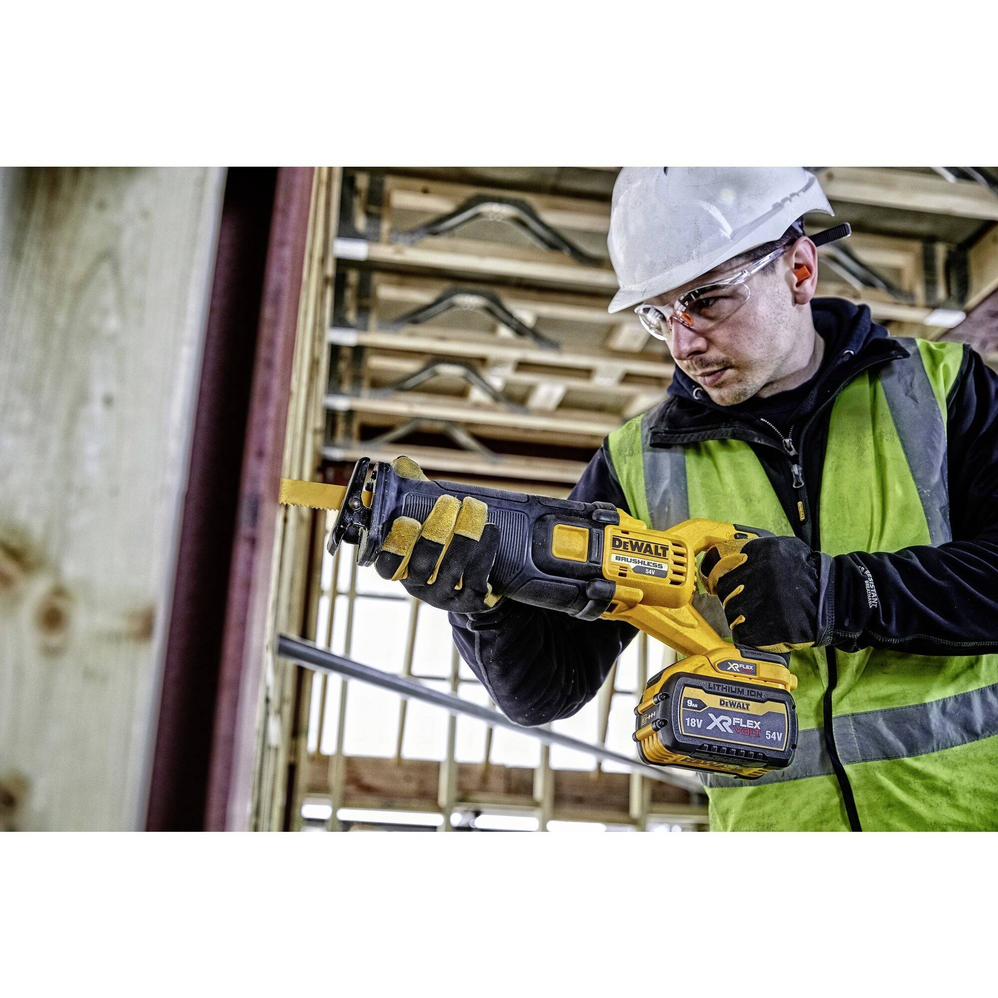Un ouvrier portant des équipements de protection utilise un outil électrique pour scier une pièce de bois sur un chantier de construction.