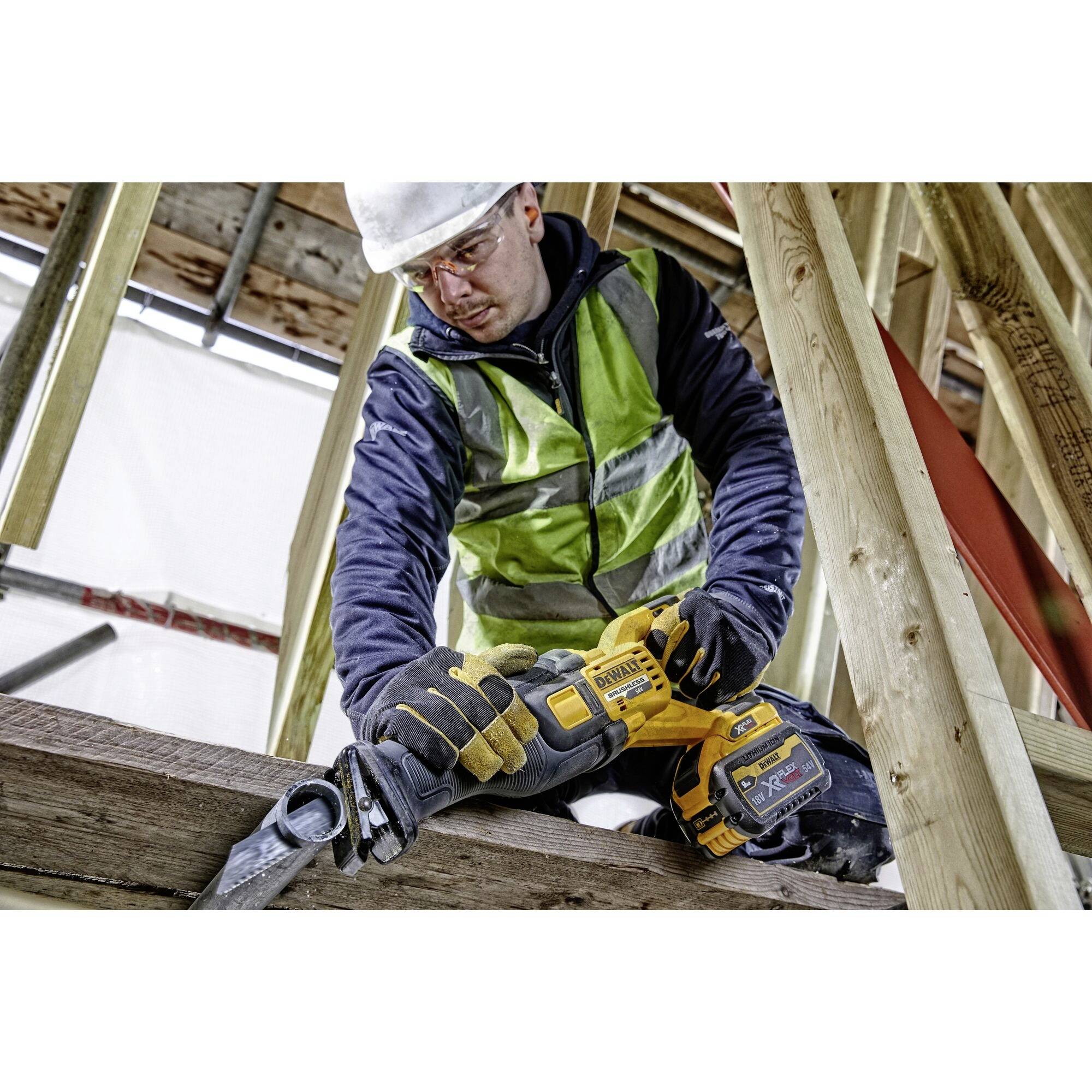 Un ouvrier portant un équipement de protection utilise une scie électrique pour couper du bois dans un bâtiment en cours de construction.