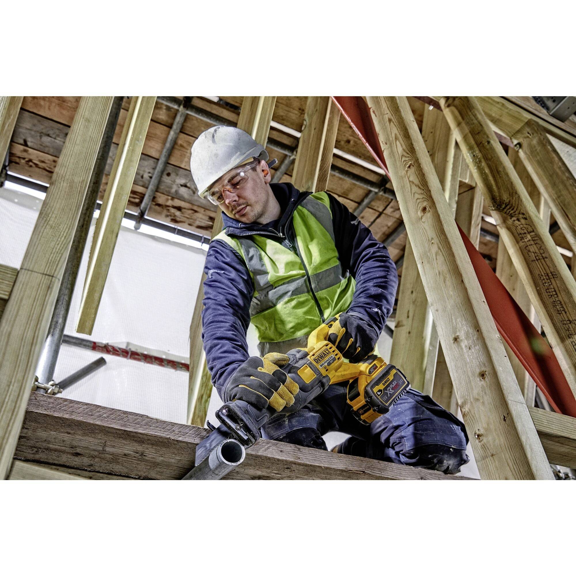 Un ouvrier portant un gilet de sécurité et un casque travaille avec concentration à l'aide d'un outil électrique sur une structure en bois.