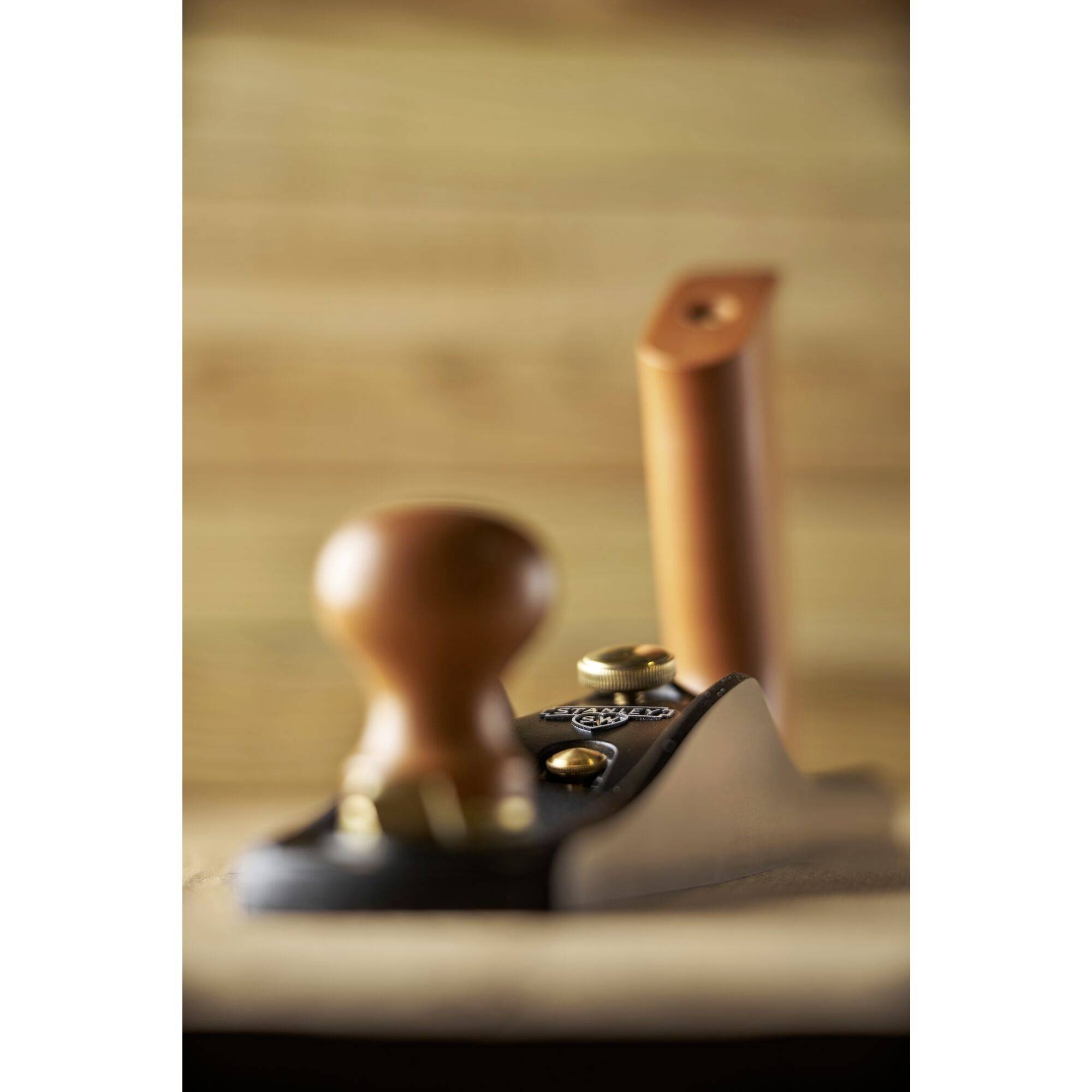 Un rabot à main en bois se concentre au premier plan, avec un arrière-plan flou de surfaces en bois.
