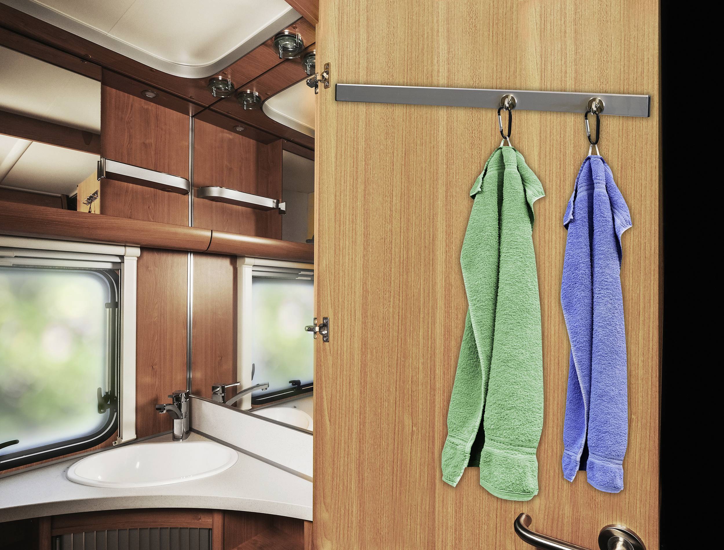 Salle de bain dans un camping-car avec deux serviettes suspendues à la porte et un lavabo avec un miroir en arrière-plan.