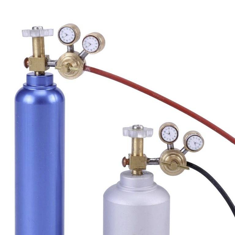 Deux bouteilles de gaz équipées de détendeurs et de manomètres, l'une bleue et l'autre blanche, reliées par des tuyaux rouges.
