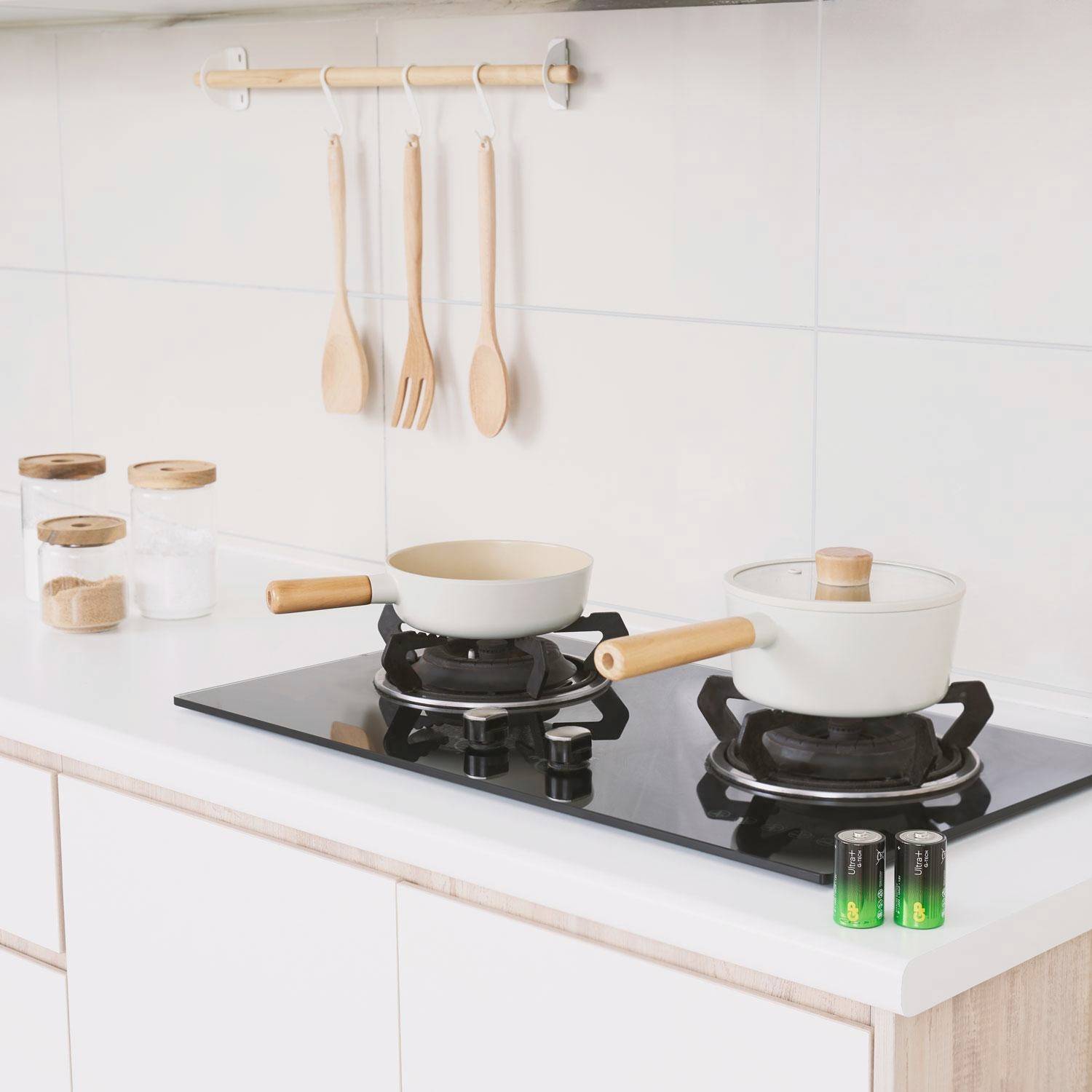 Cuisine lumineuse et moderne avec deux foyers de cuisson, des poêles sur la cuisinière, des cuillères en bois au mur et des bocaux de rangement sur le plan de travail.