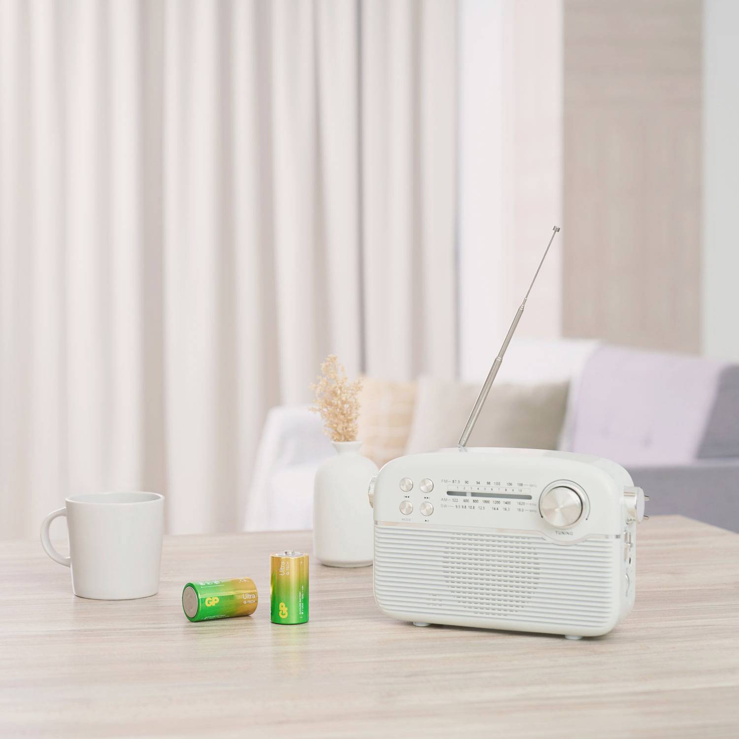 Radio rétro blanc sur une table à côté d'une tasse et deux piles dans un salon lumineux.
