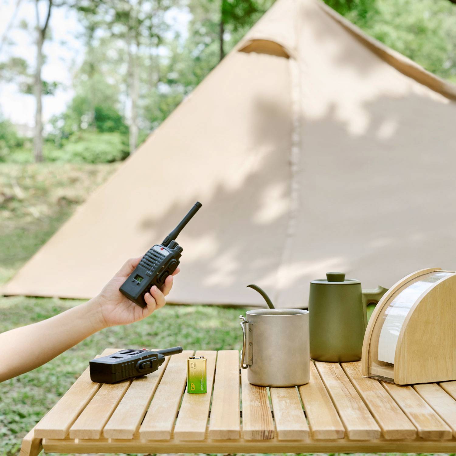 Une table avec une radio, une tasse et une boîte à pain devant une tente en extérieur. Scène atmosphérique d'un terrain de camping.