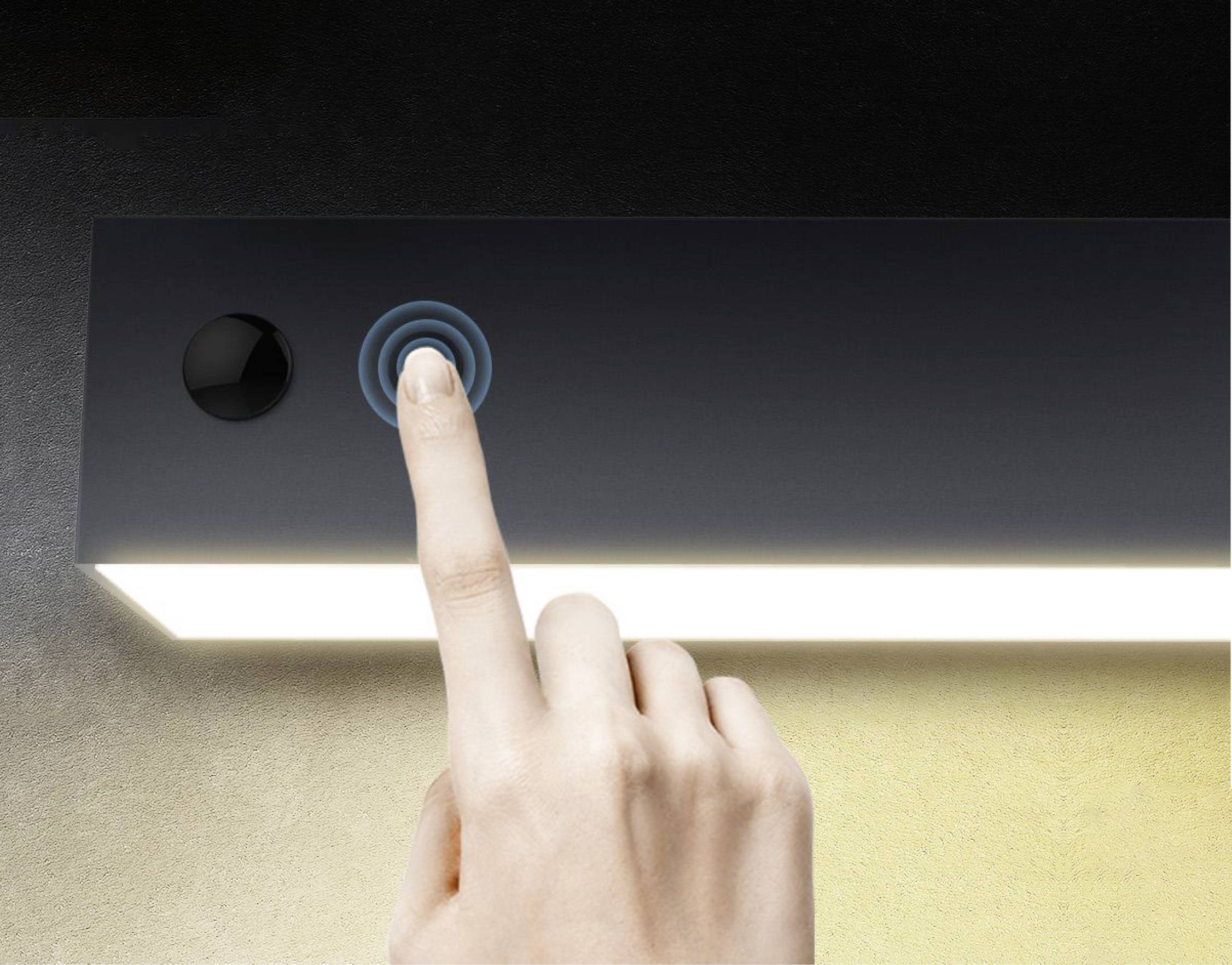 Une main appuie sur un bouton-capteur d'une lampe rectangulaire lumineuse pour l'activer ou la désactiver.