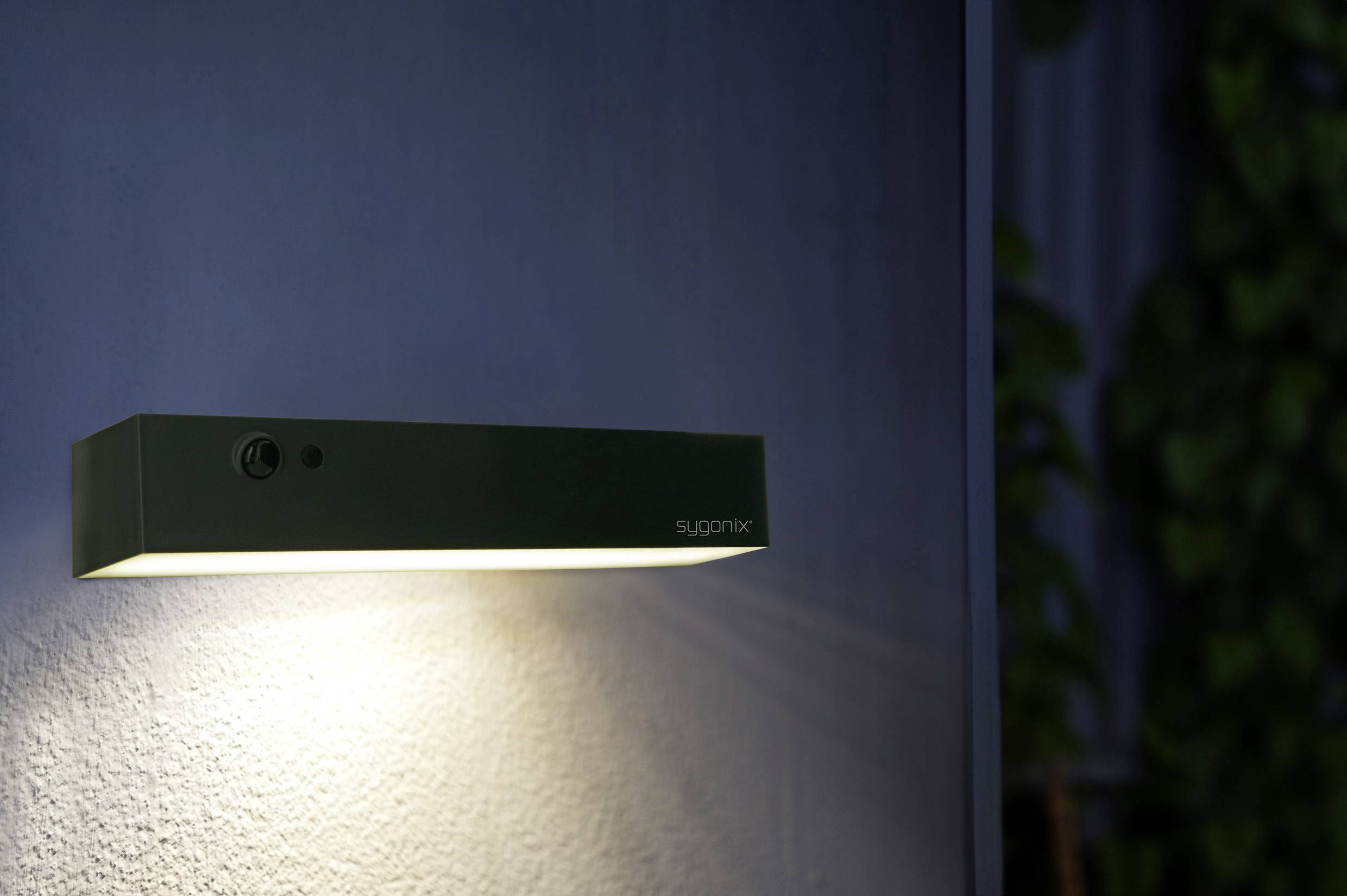 Une lampe rectangulaire et moderne projette une lumière chaleureuse sur un mur.