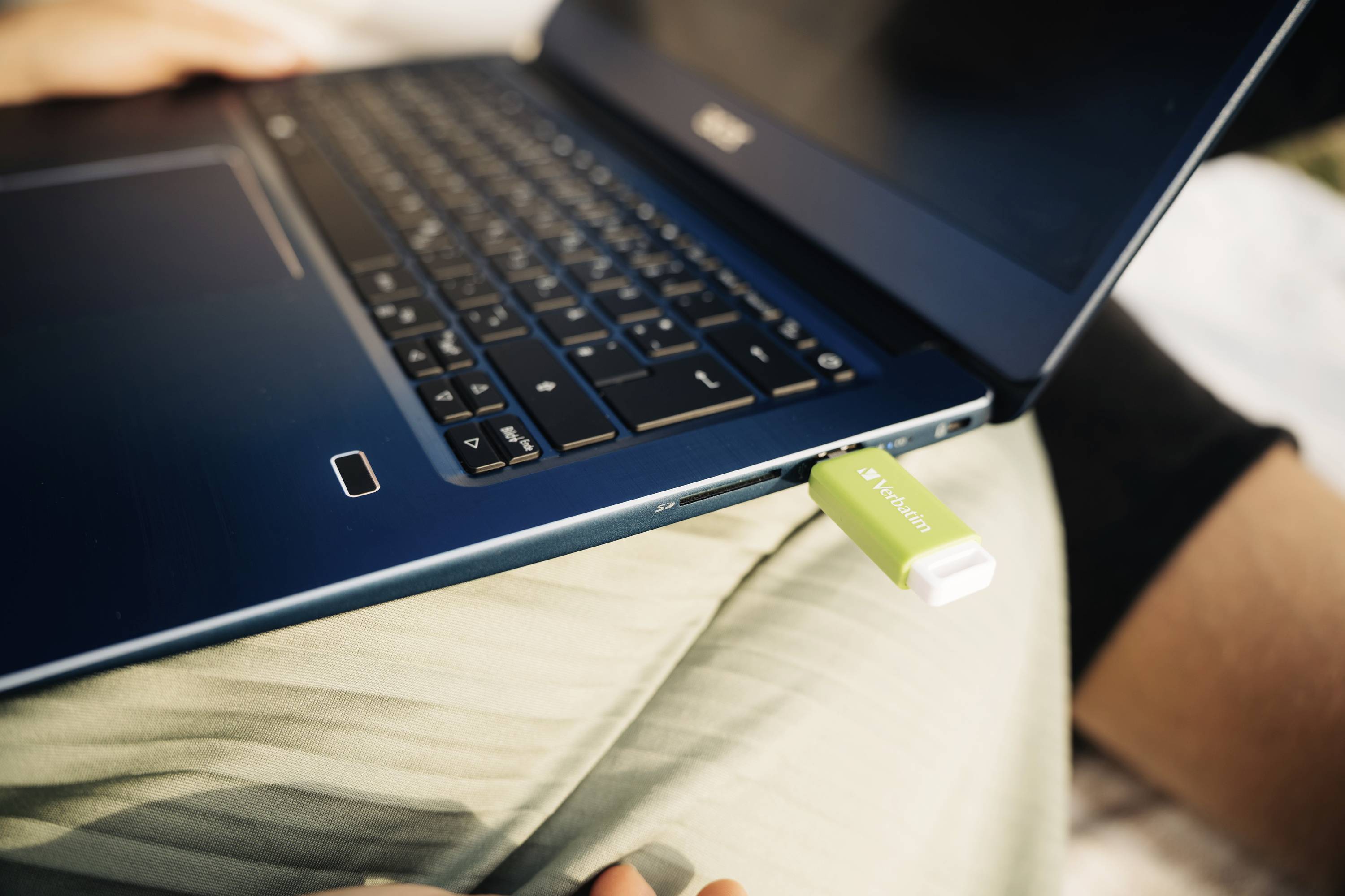 Une clé USB verte est branchée dans un ordinateur portable bleu, posé sur une surface claire.