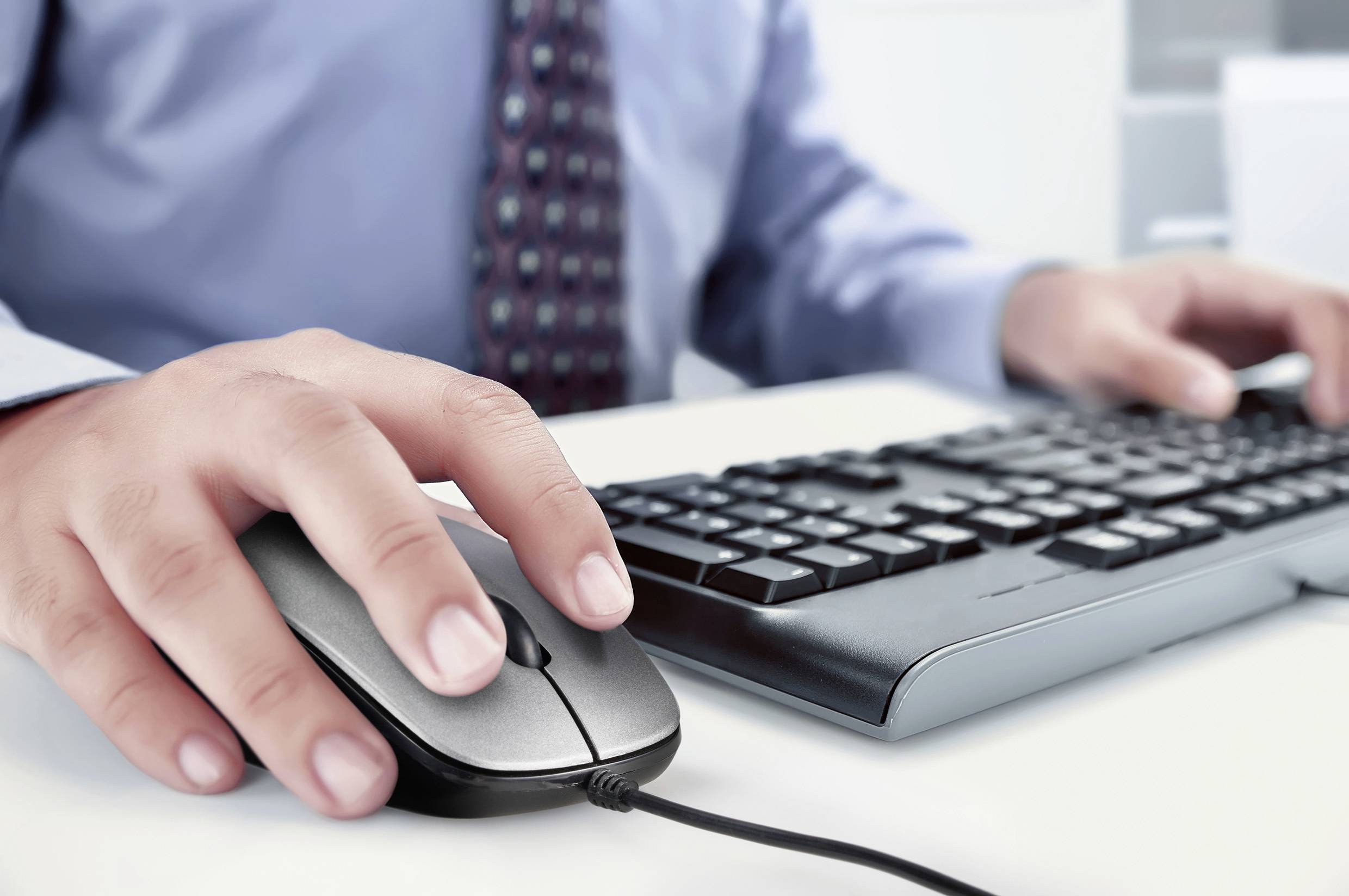 Une personne travaille sur un ordinateur, regardant l'écran, tenant une souris dans sa main droite et sa main gauche posée sur le clavier.