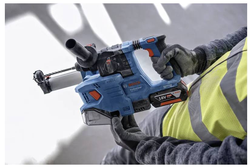 Une personne portant un gilet de sécurité tient un marteau perforateur sans fil Bosch 18V de couleur bleue, prêt à être utilisé dans un chantier de construction ou de rénovation.