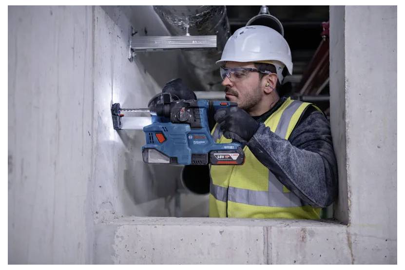 Un ouvrier du bâtiment portant un équipement de sécurité utilise une perceuse électrique sur un mur en béton, concentré et soucieux de la précision.