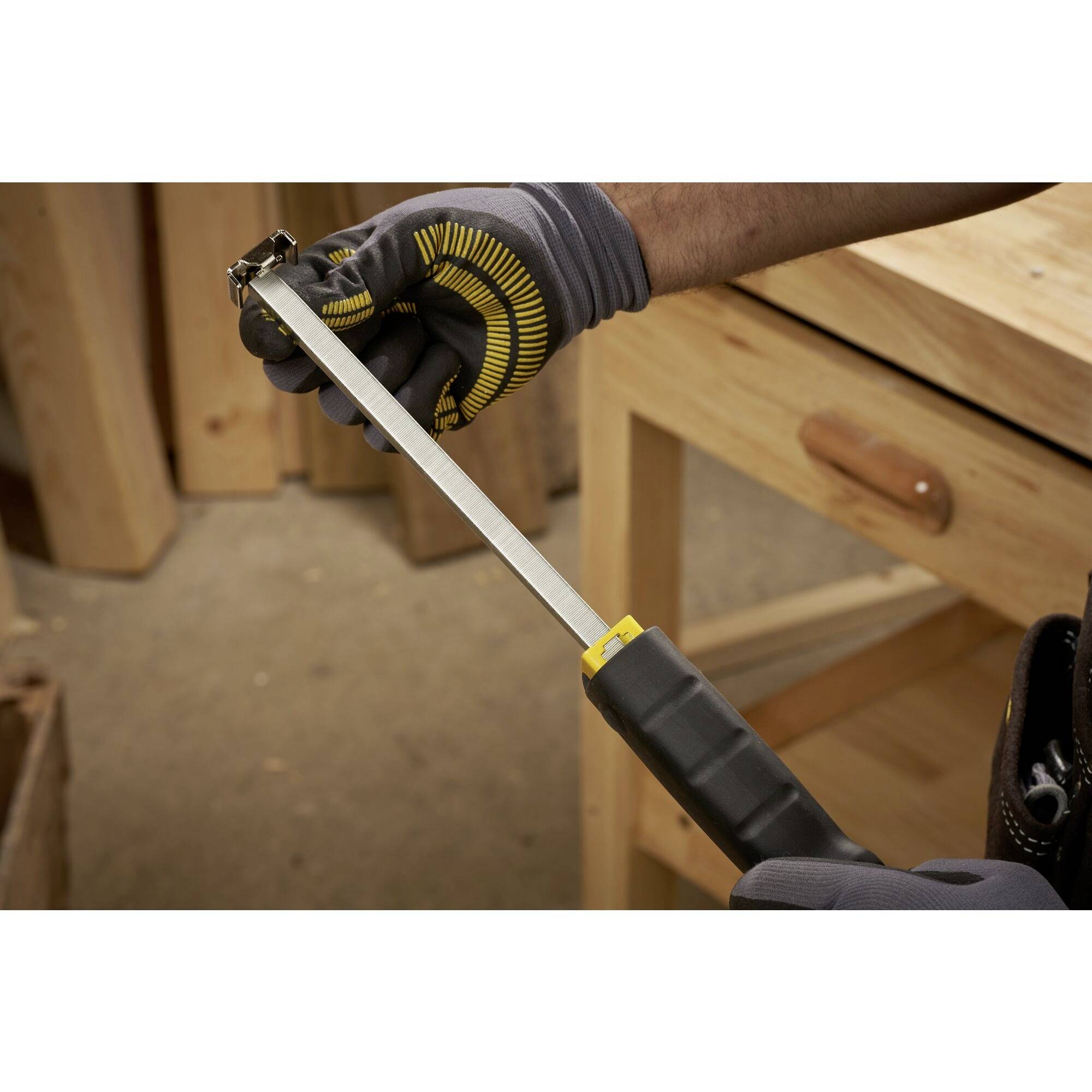 Une personne portant des gants utilise une lime métallique pour travailler un petit objet métallique sur un établi.
