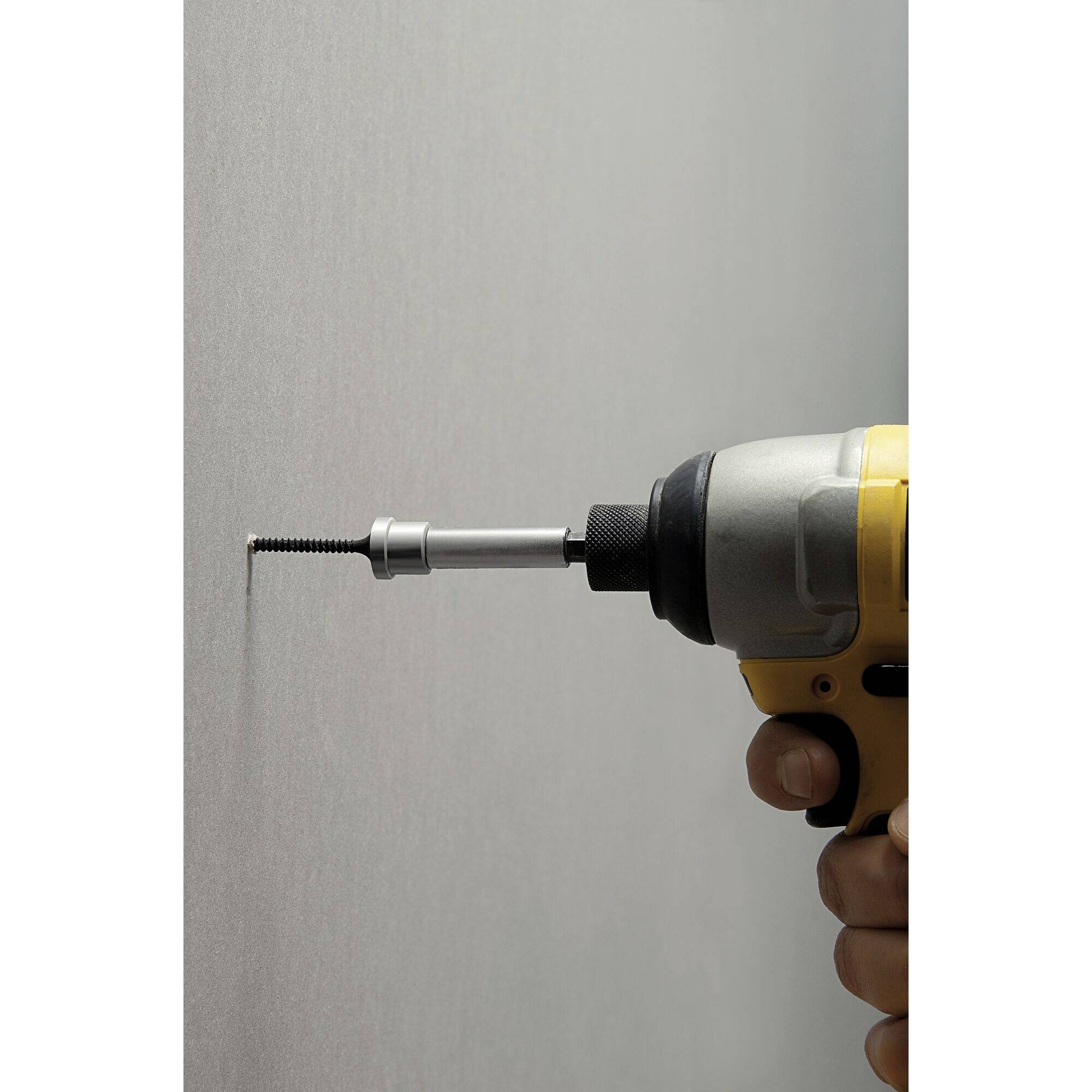 Une main tient une perceuse jaune qui enfonce une vis dans un mur gris.
