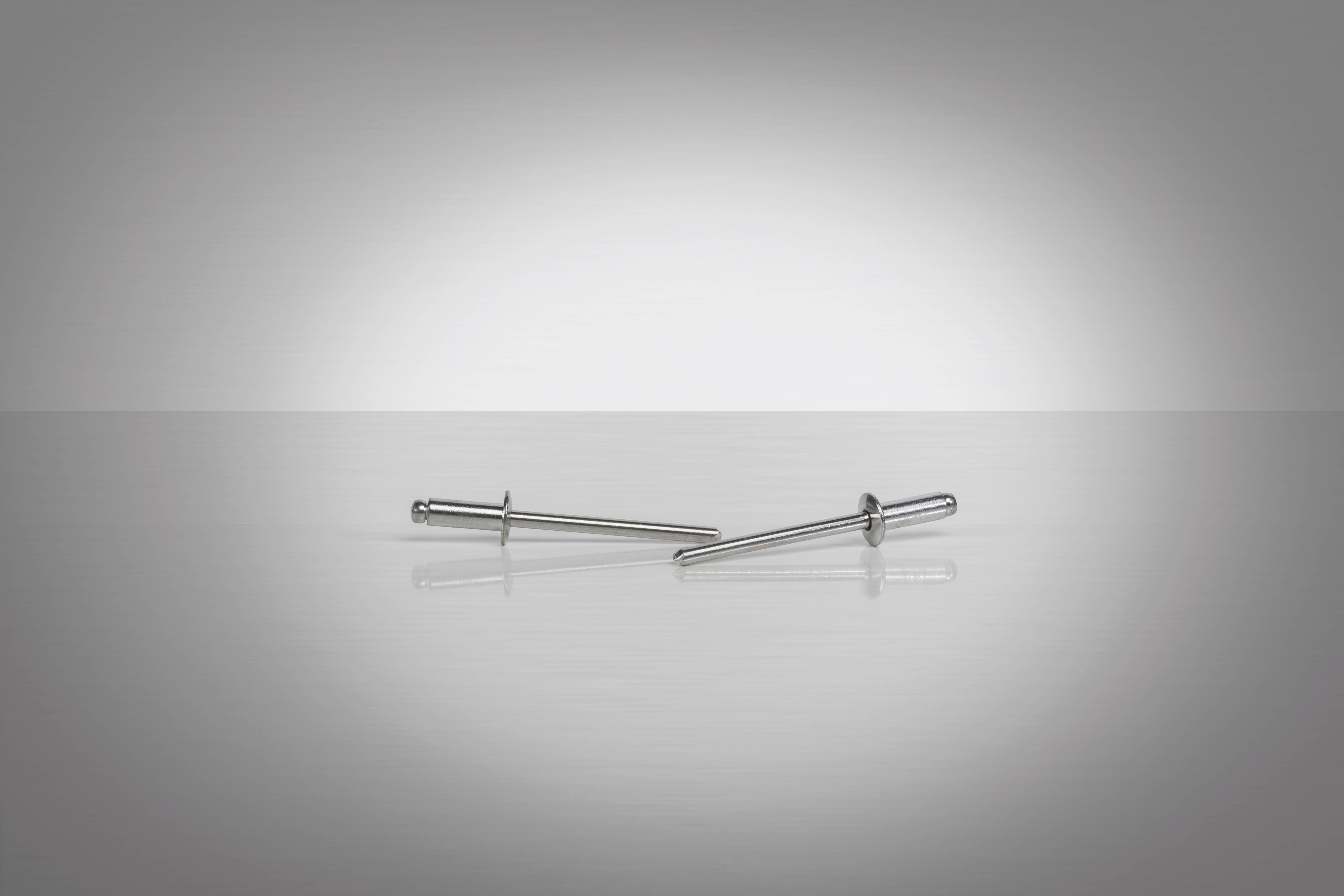 Deux rivets en argent reposent sur une surface lisse et grise, disposés horizontalement.