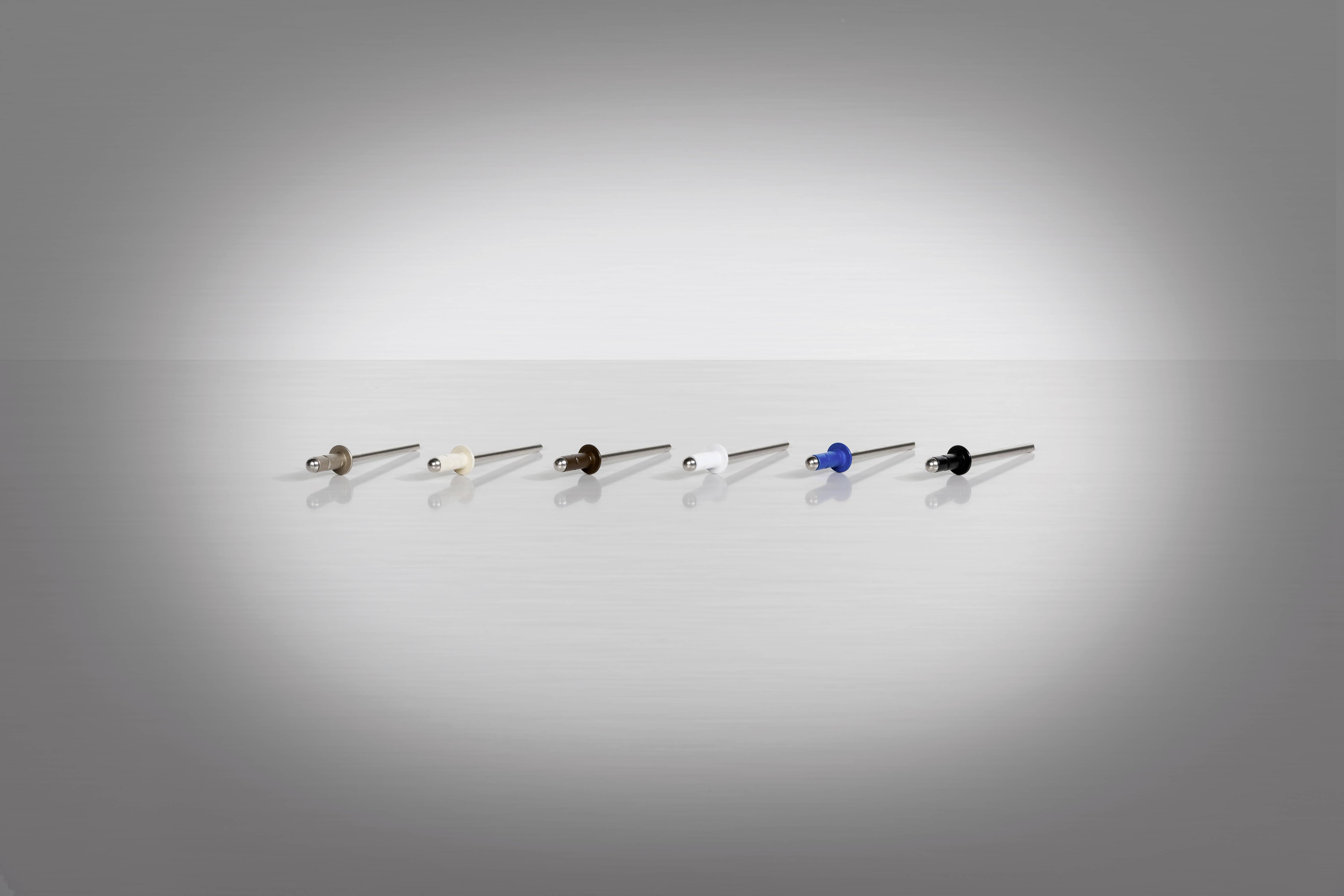 Six punaises de couleurs différentes alignées sur une surface brillante et réfléchissante devant un fond neutre.