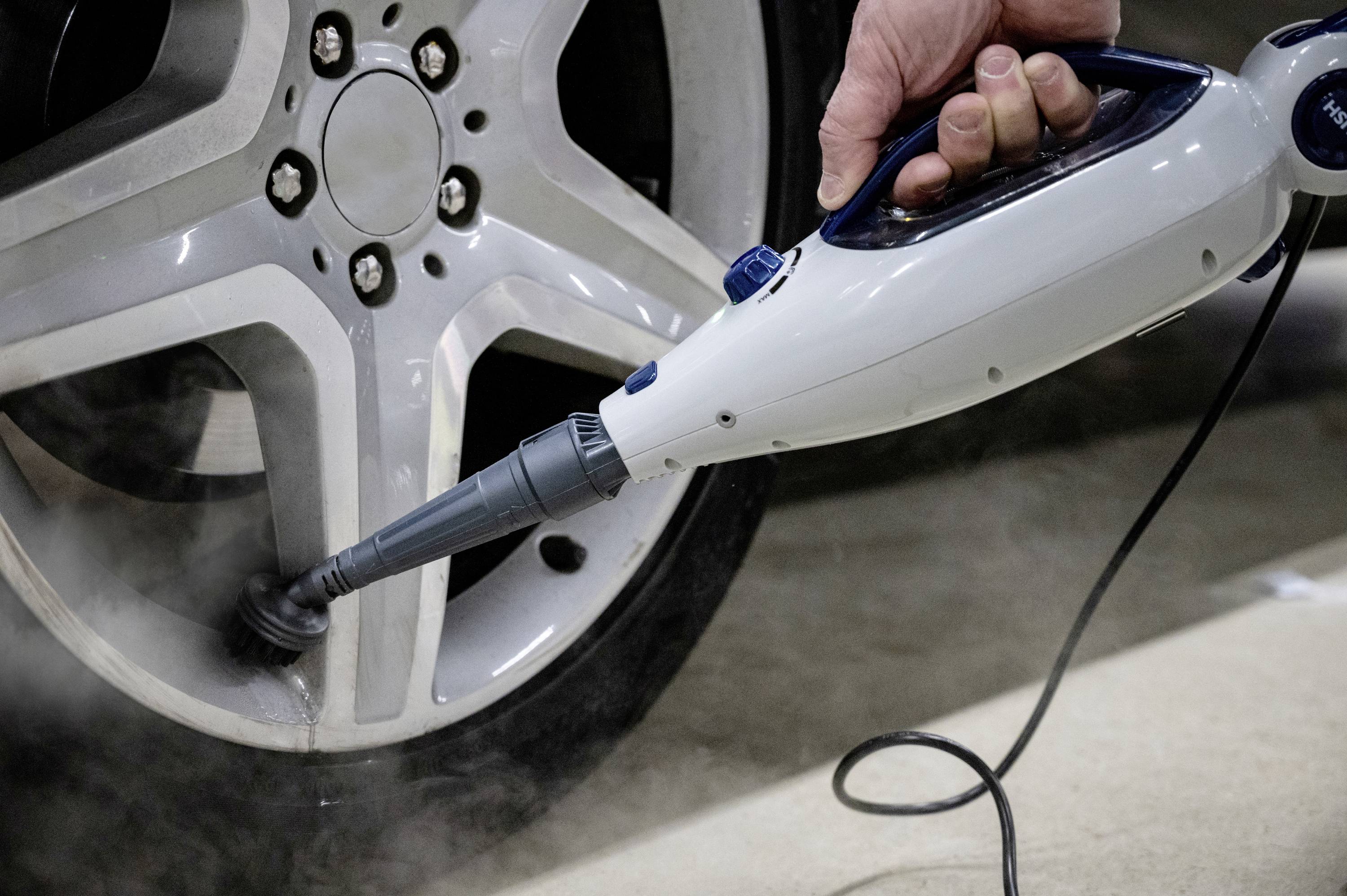 Une personne nettoie une jante de roue de voiture avec un nettoyeur à vapeur. La vapeur élimine les saletés des boulons de roue et de la jante.