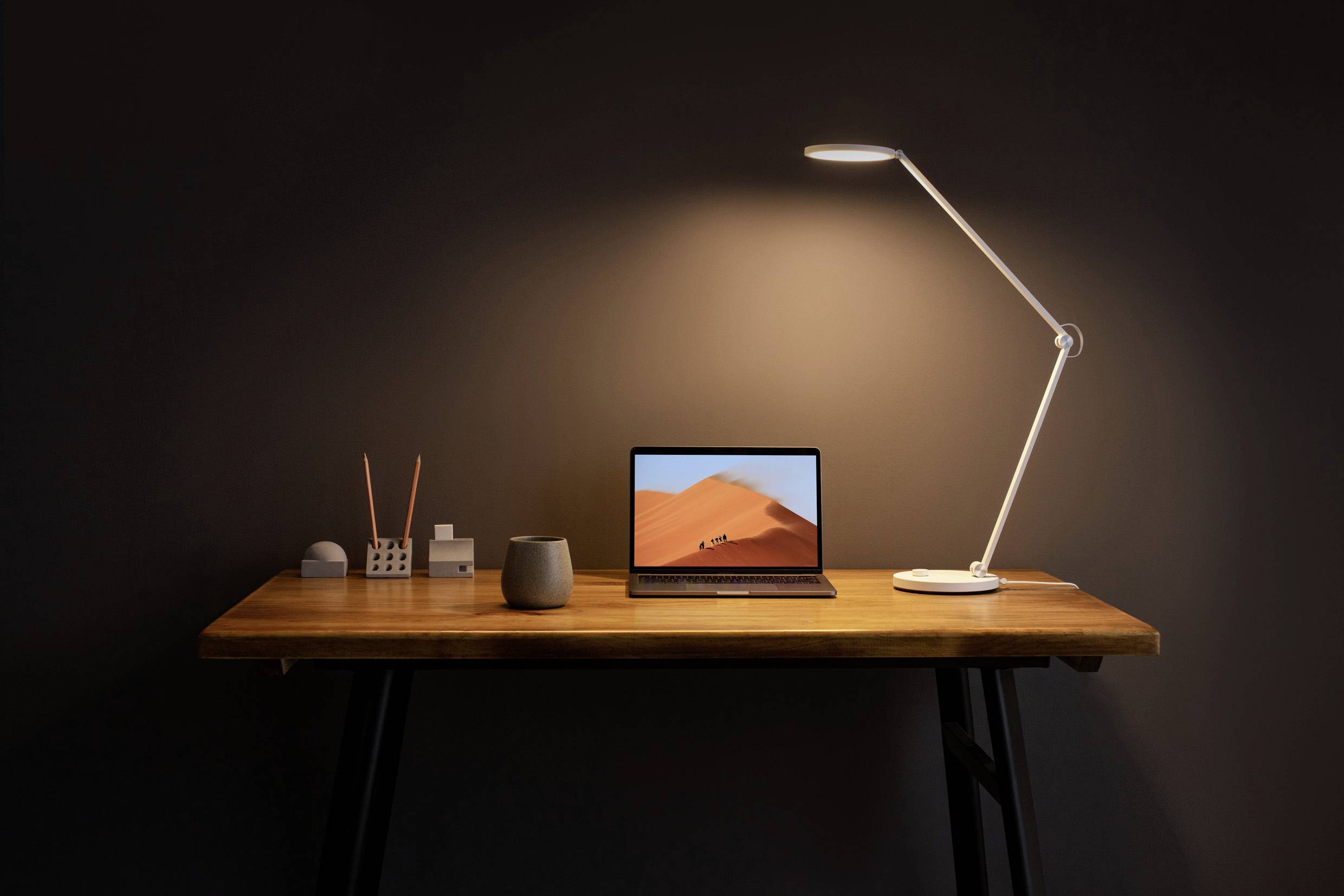 Un bureau minimaliste avec un ordinateur portable ouvert, une lampe de bureau moderne et de petits accessoires de bureau sur une surface en bois.