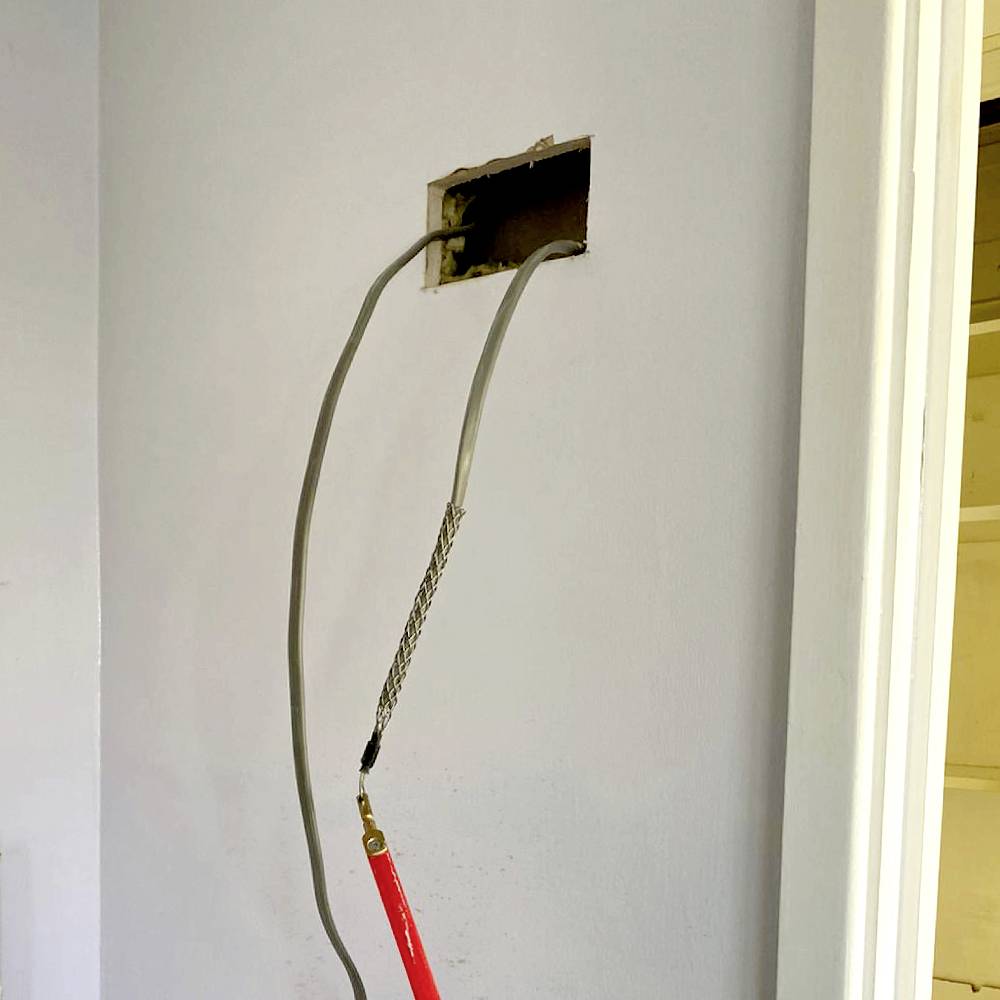 Une ouverture dans le mur avec un faisceau de câbles en saillie et l'outillage approprié. L'environnement suggère des travaux d'installation électrique en cours.