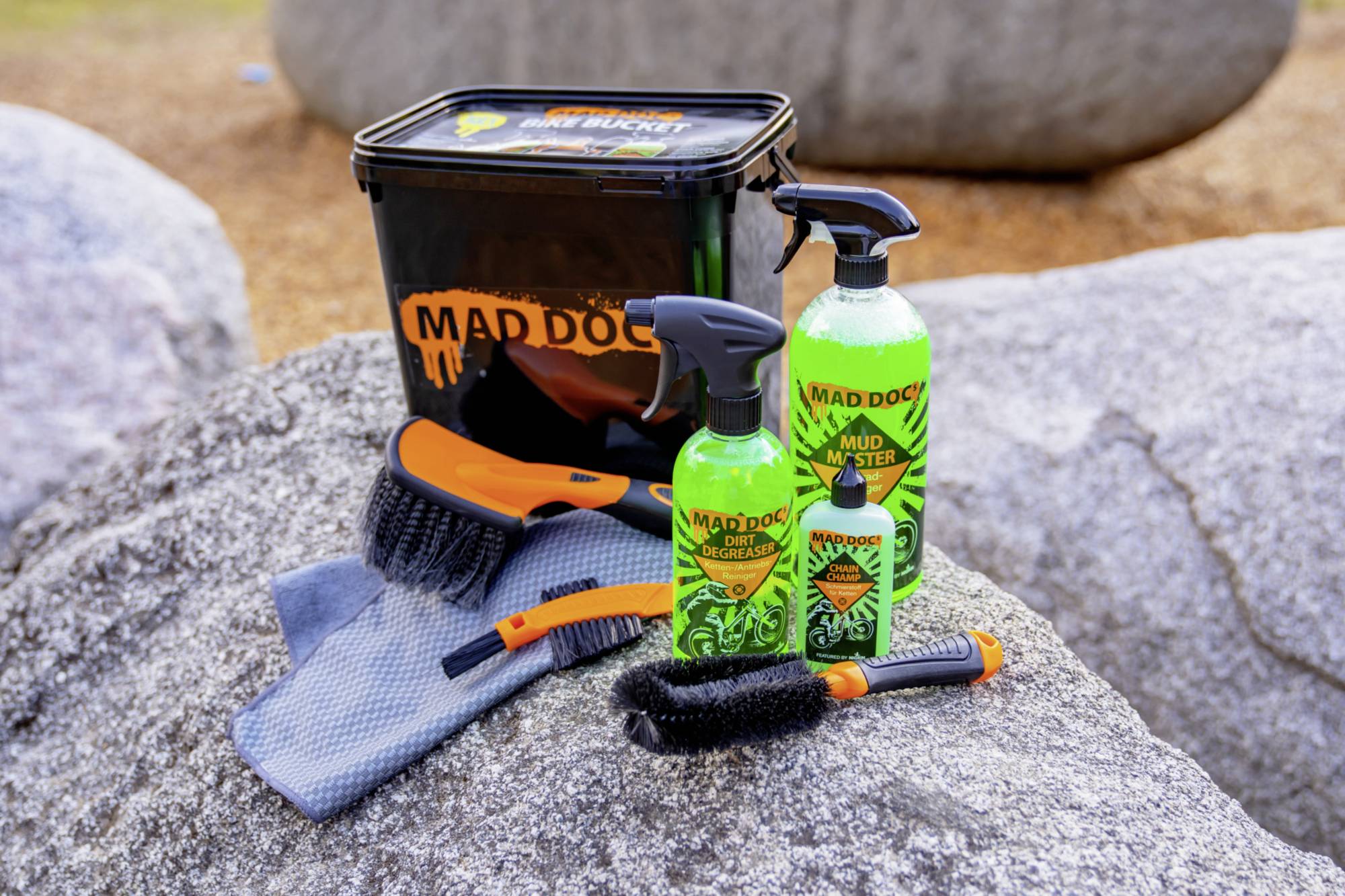 Ensemble de nettoyage sur une pierre : un seau avec le logo 'Mad Doc', deux brosses, un chiffon et deux bouteilles de produit de nettoyage.