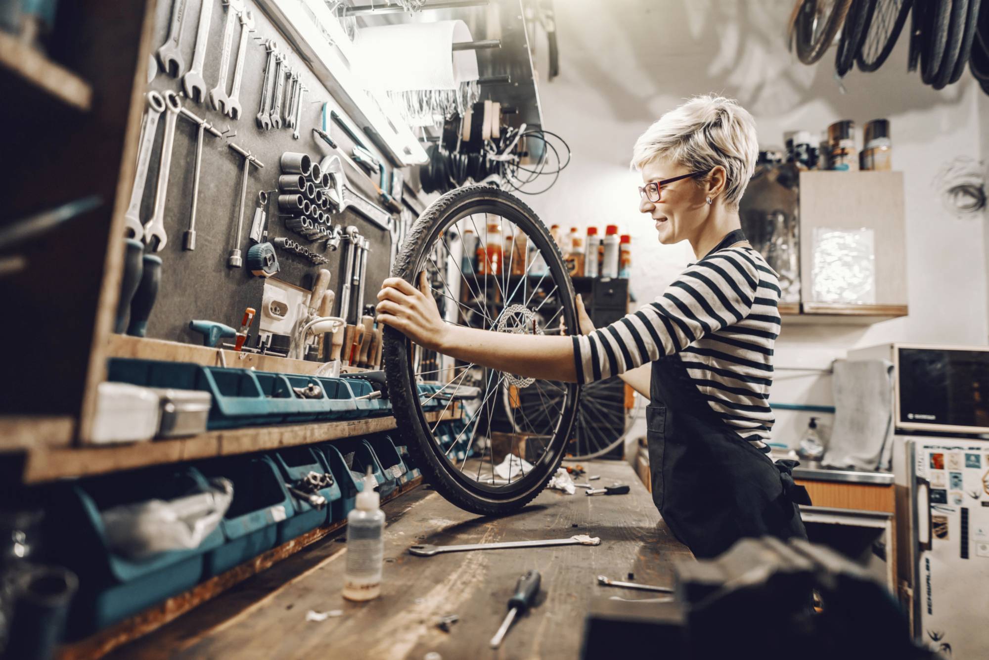 Une personne répare un vélo dans un atelier. Des outils et des pièces de rechange sont visibles en arrière-plan.