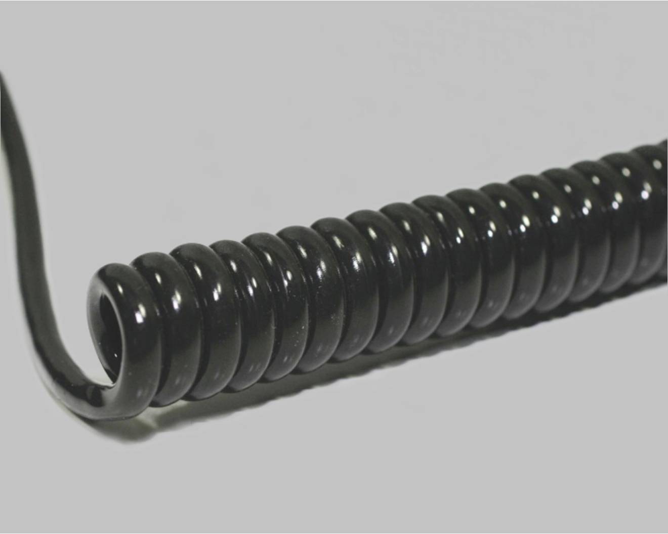 Un câble spiralé noir est posé sur une surface grise. Il est enroulé serré et forme une forme bouclée.