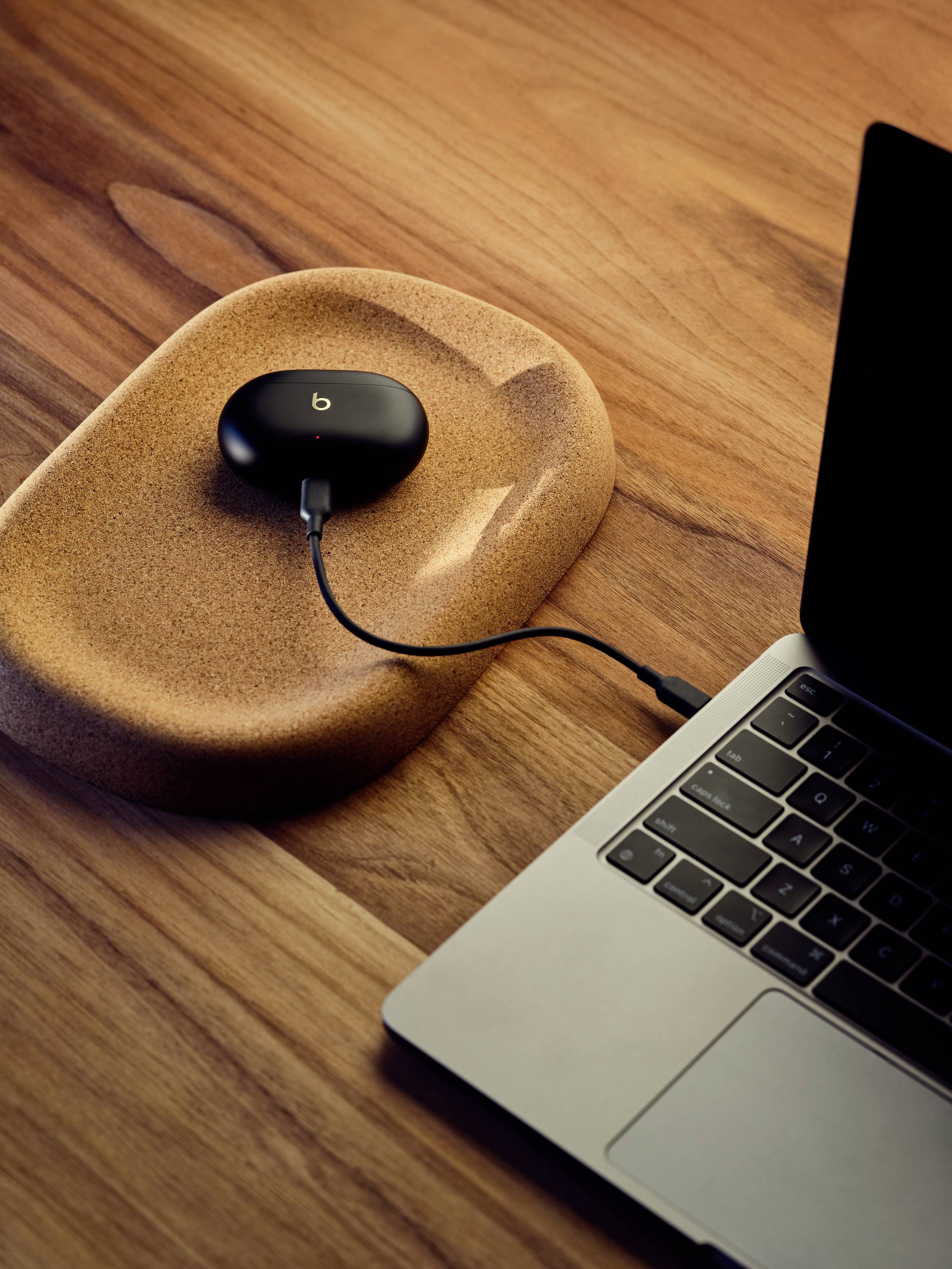 Un ordinateur portable est posé sur une table en bois, à côté duquel un petit appareil noir et rond est en charge.