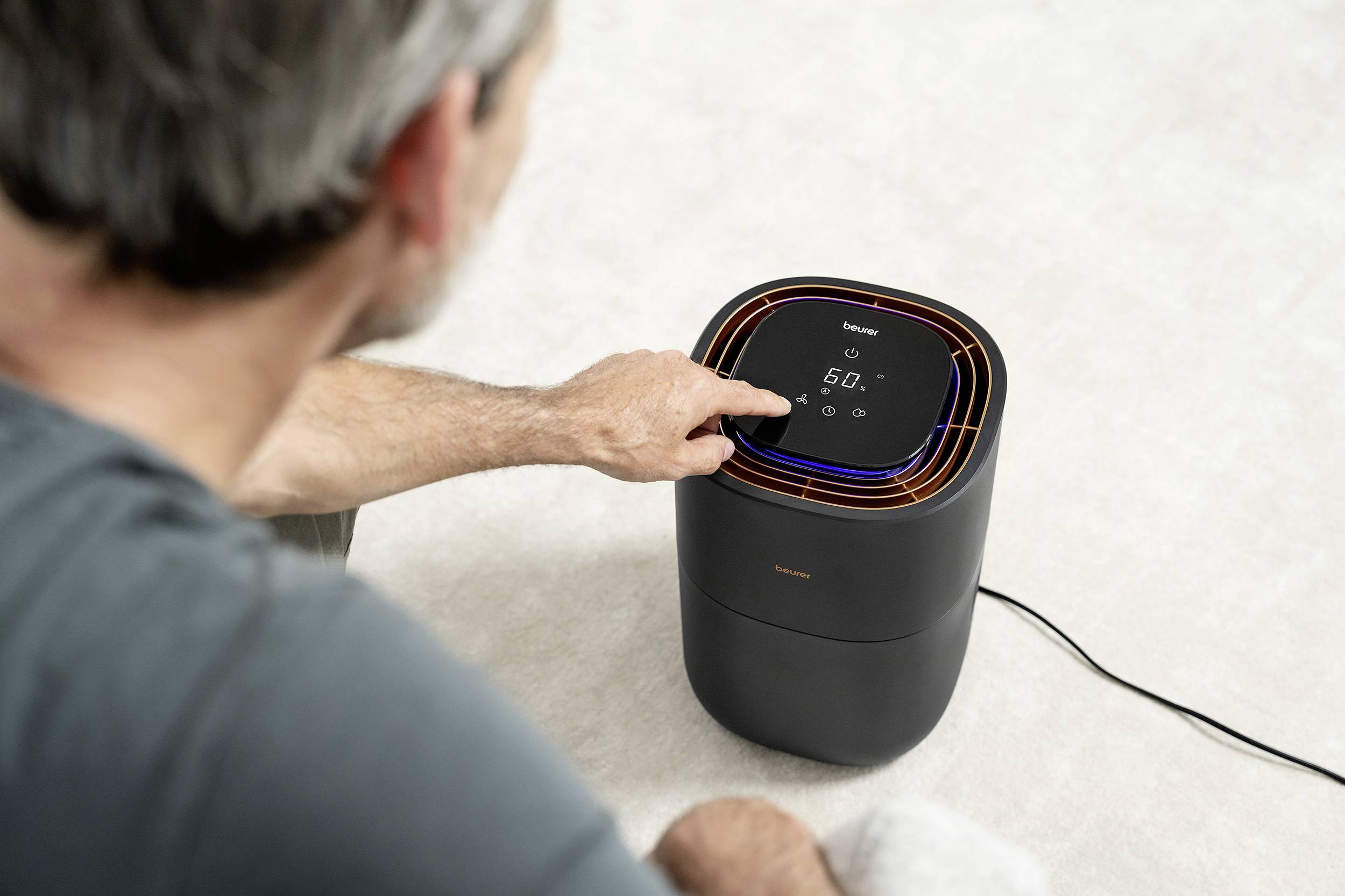 Une personne utilise un appareil compact noir doté d'un écran et de touches tactiles, probablement un purificateur d'air ou un ventilateur.